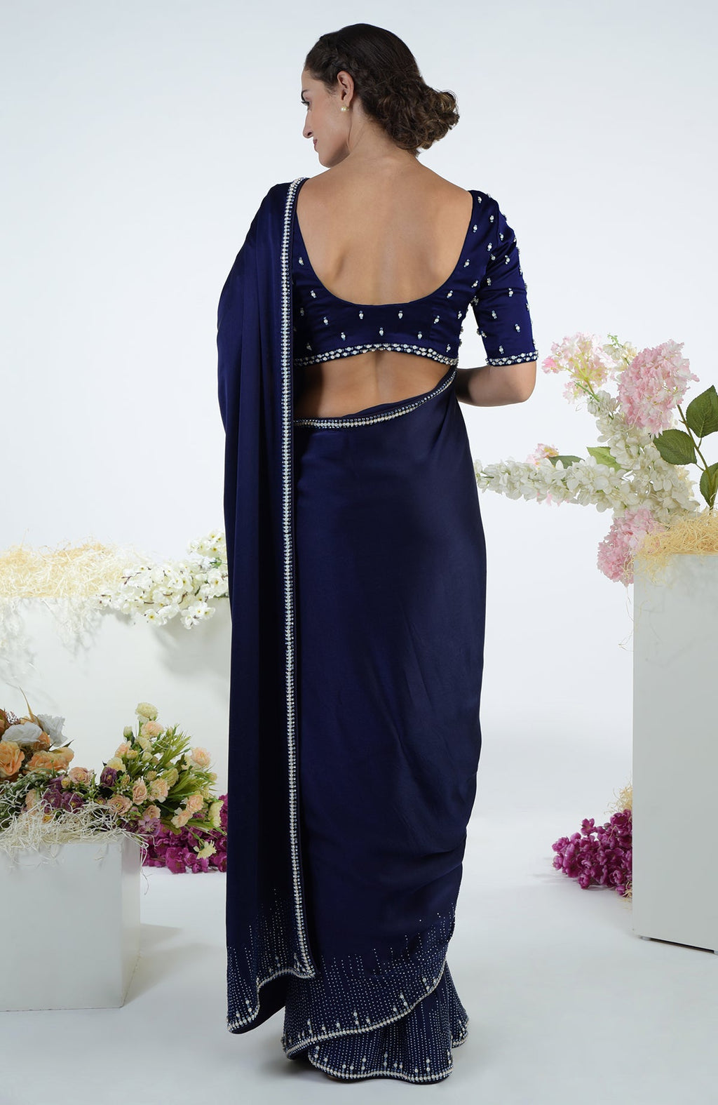A woman models a midnight blue crystal hand-embroidered saree and blouse from the back.