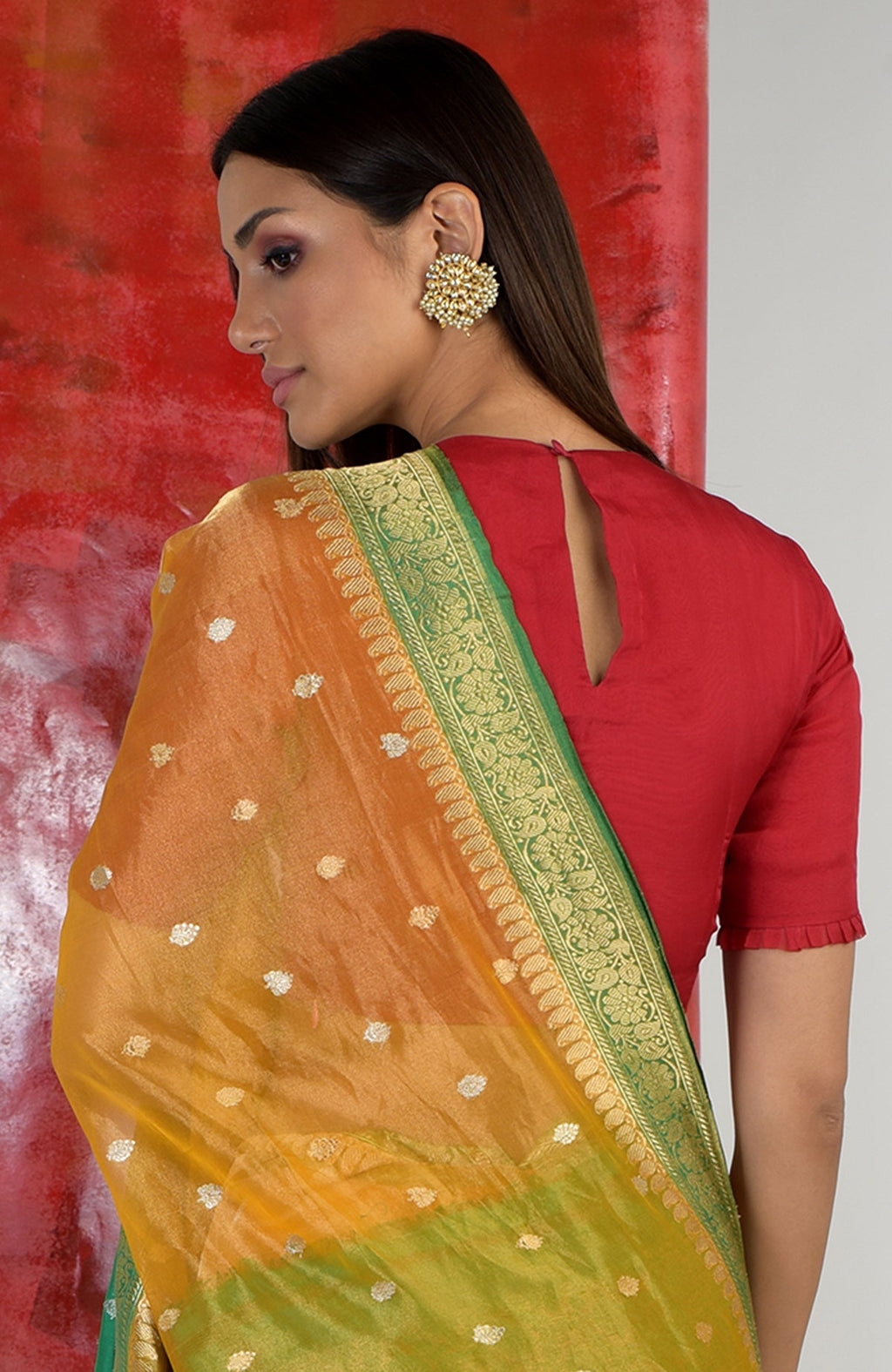 Red blouse with a keyhole back and ruffled sleeves, paired with a gold and green saree.