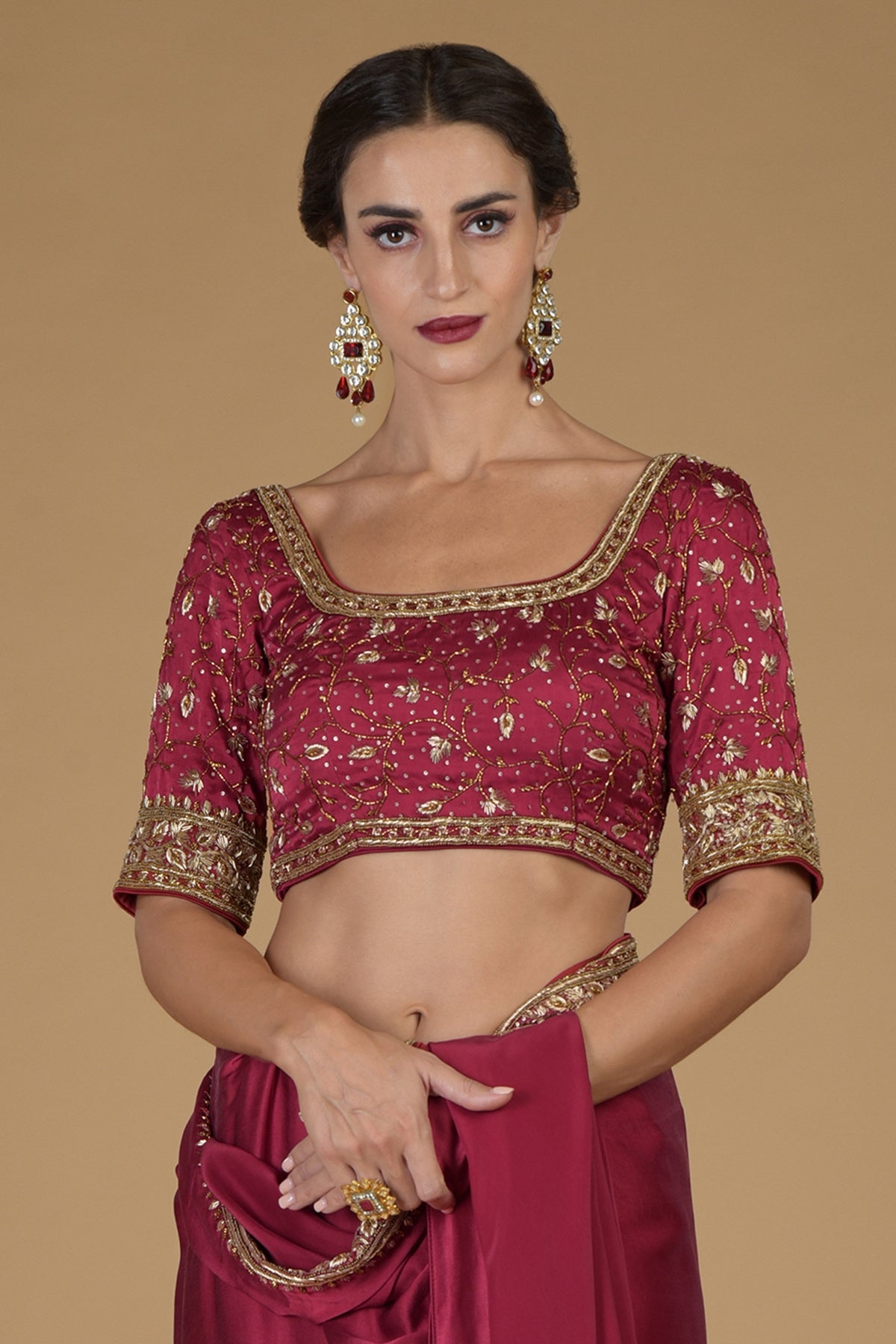 Maroon U neck hand-embroidered zardozi blouse with gold and red earrings.
