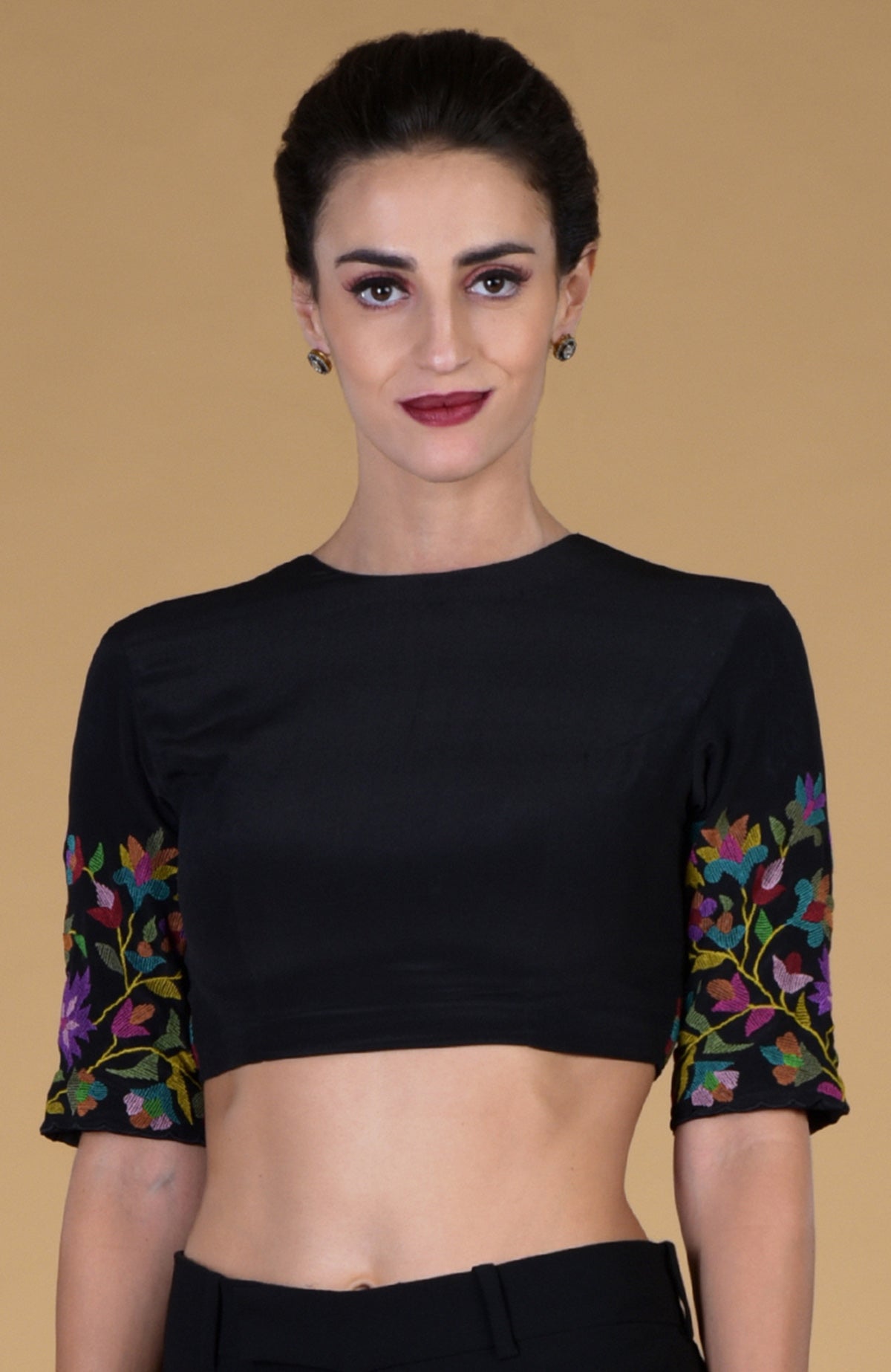 A woman models a black crop top with colorful floral embroidery on the sleeves.