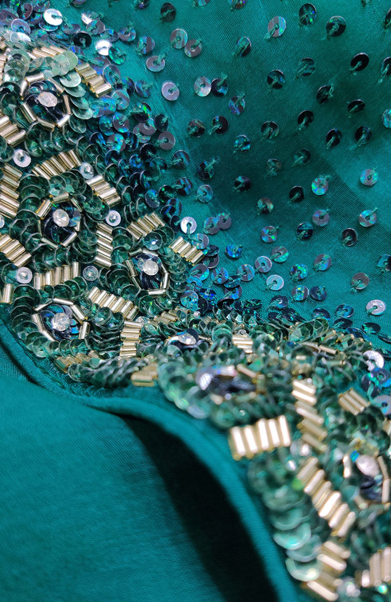 Close-up of emerald green fabric with intricate gold beads and green sequin embroidery.