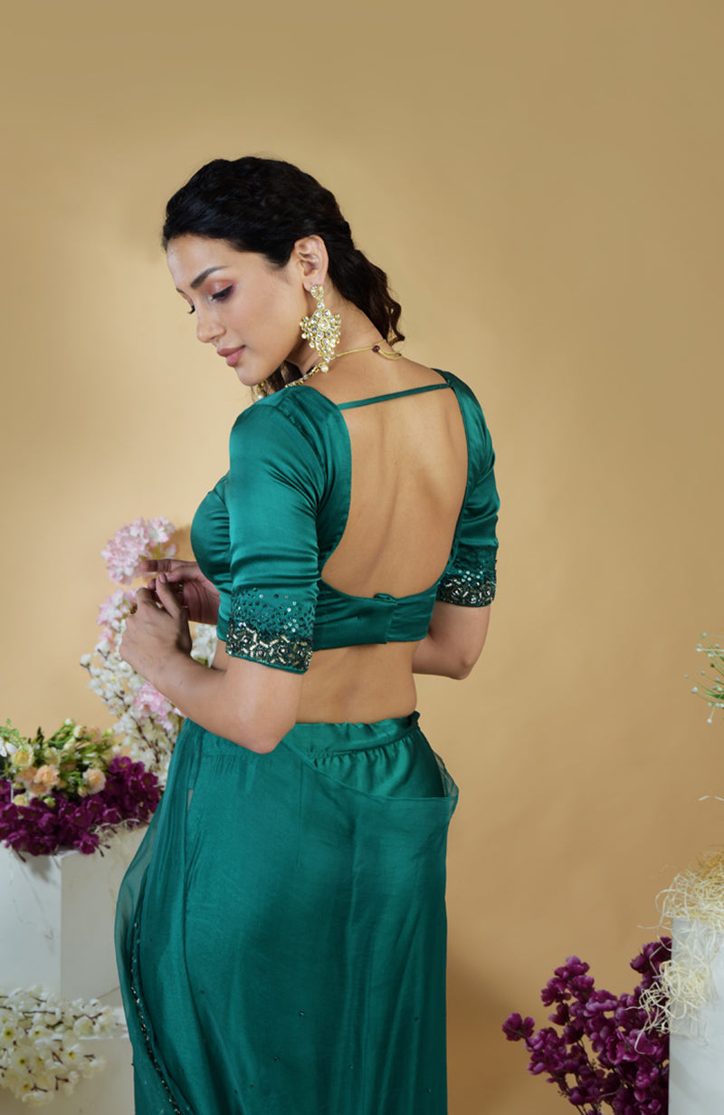 A woman in an emerald green saree with a matching blouse, featuring embroidered sleeves.