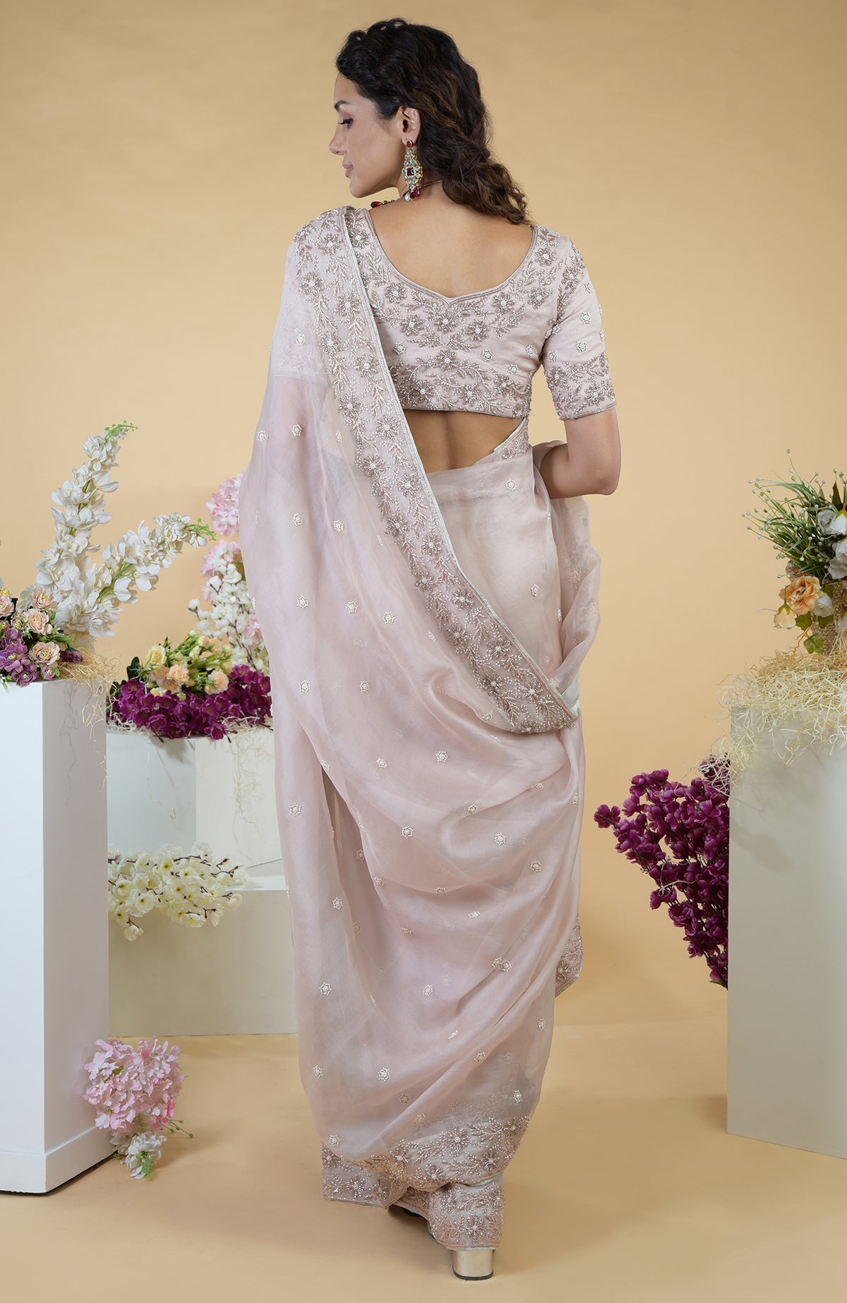 A woman from the back wears a nude pink hand-embroidered silk organza saree.