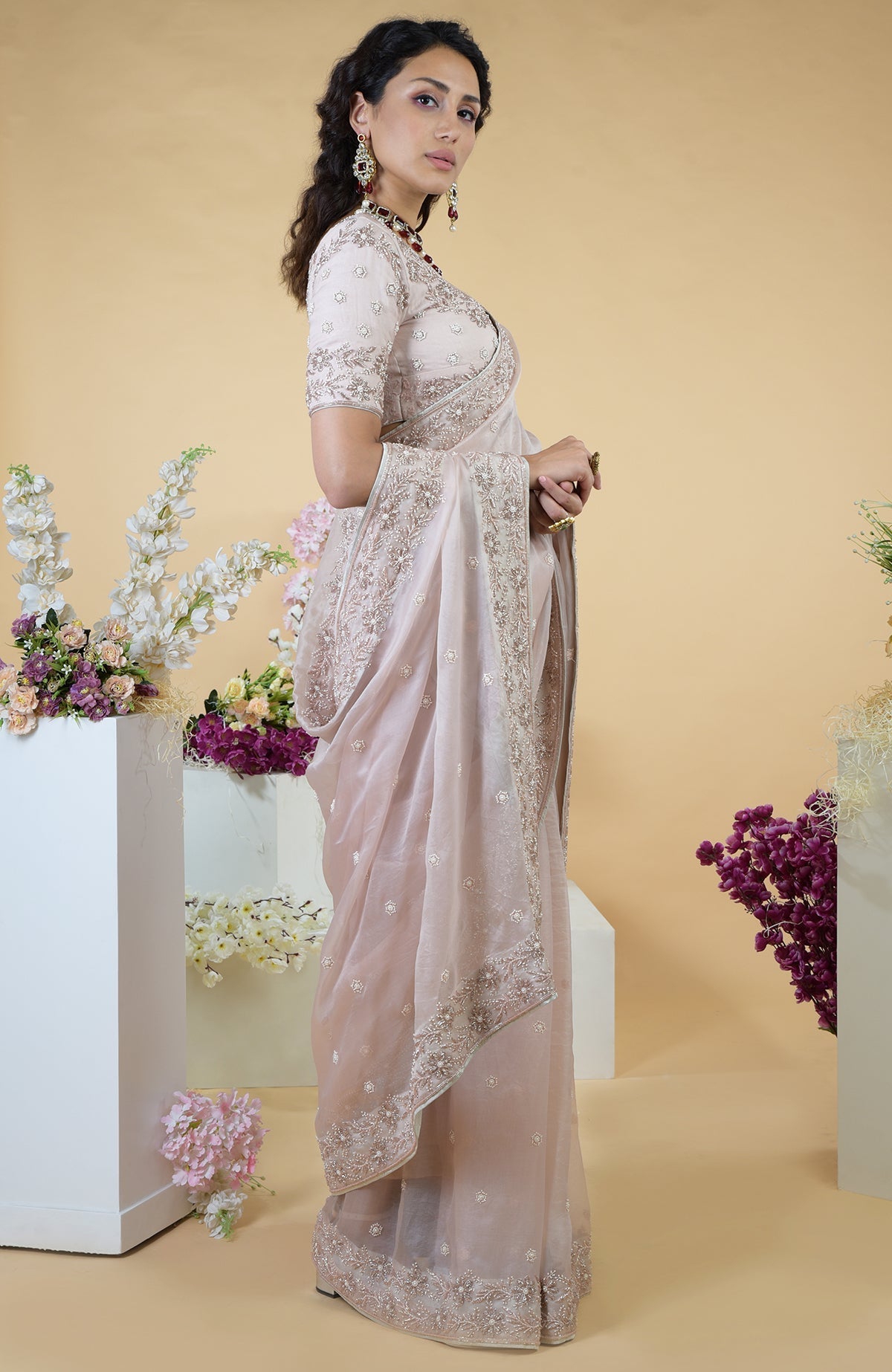 A woman models a nude pink hand-embroidered silk organza saree with a matching blouse.