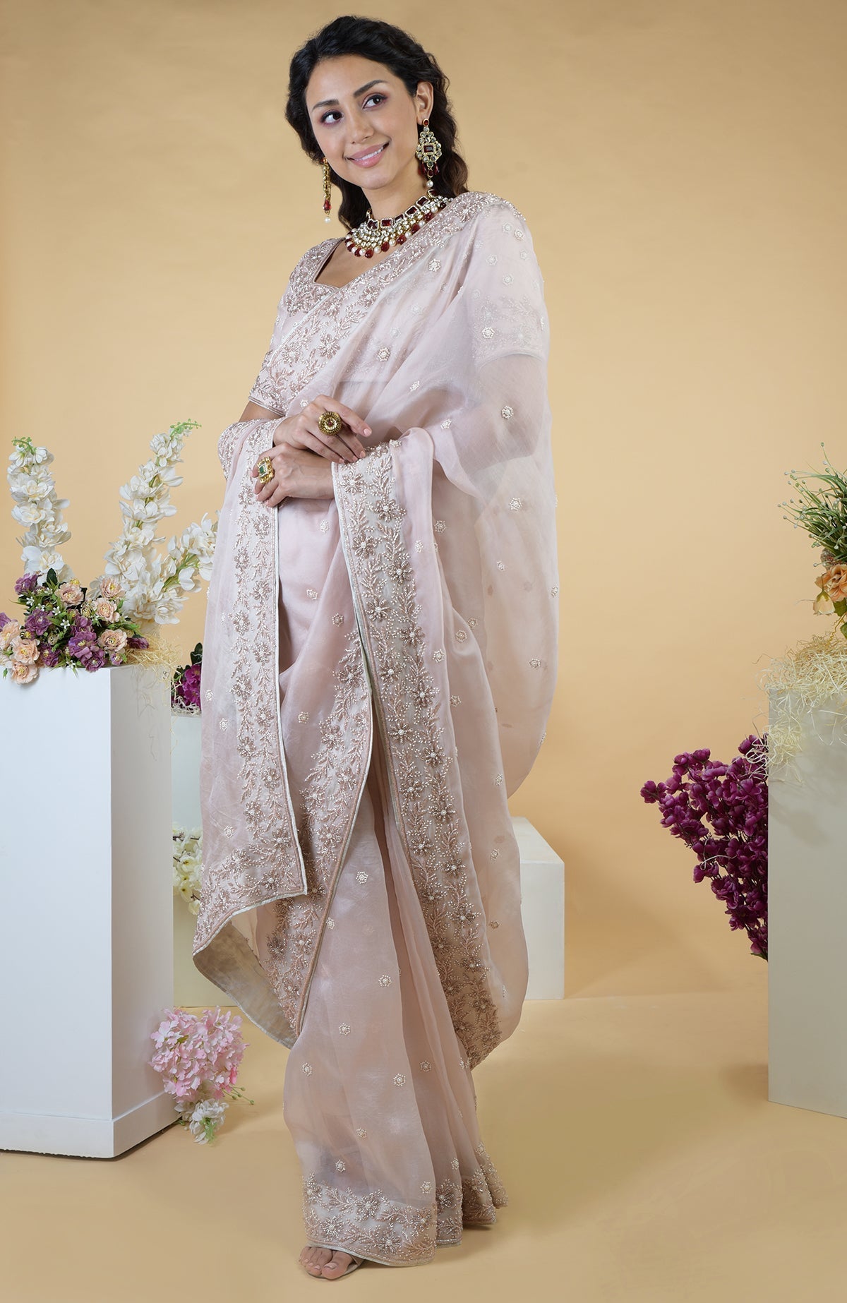 A woman models a nude pink hand-embroidered silk organza saree with floral motifs.