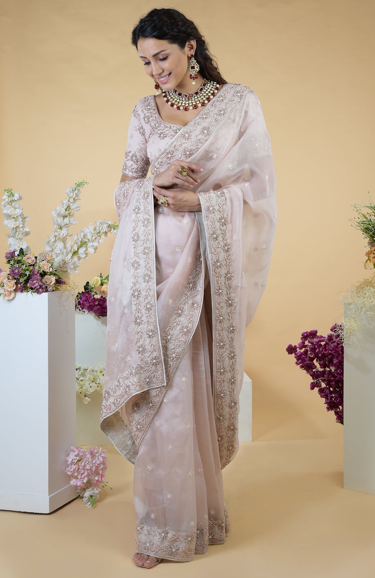 A woman models a nude pink hand-embroidered silk organza saree with jewelry.