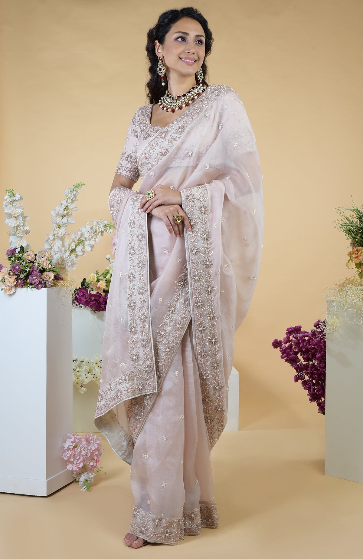 A woman models a nude pink hand-embroidered silk organza saree with floral motifs.