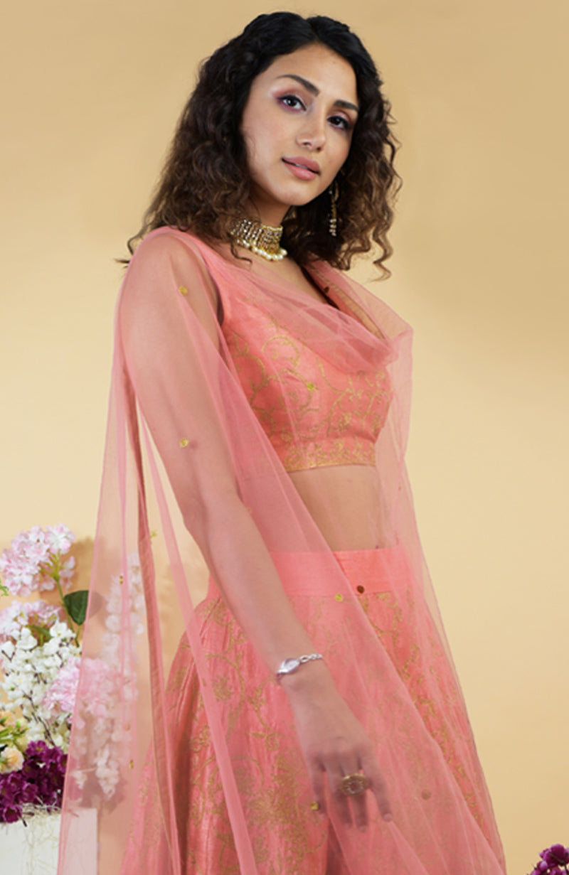 A woman models a peach lehenga set with gold embroidery and a sheer dupatta.