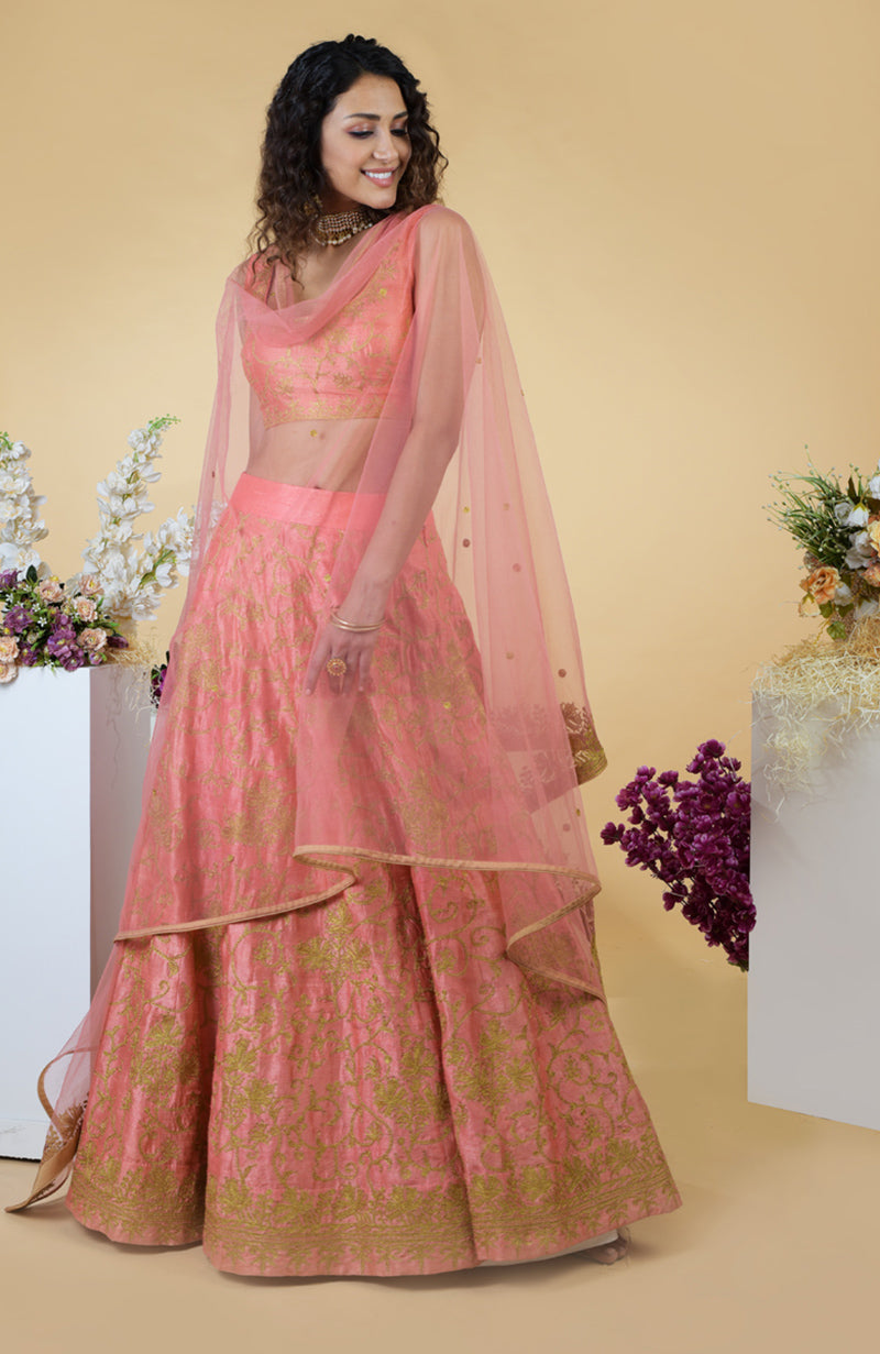 A woman models a peach lehenga set with gold embroidery and a sheer dupatta.