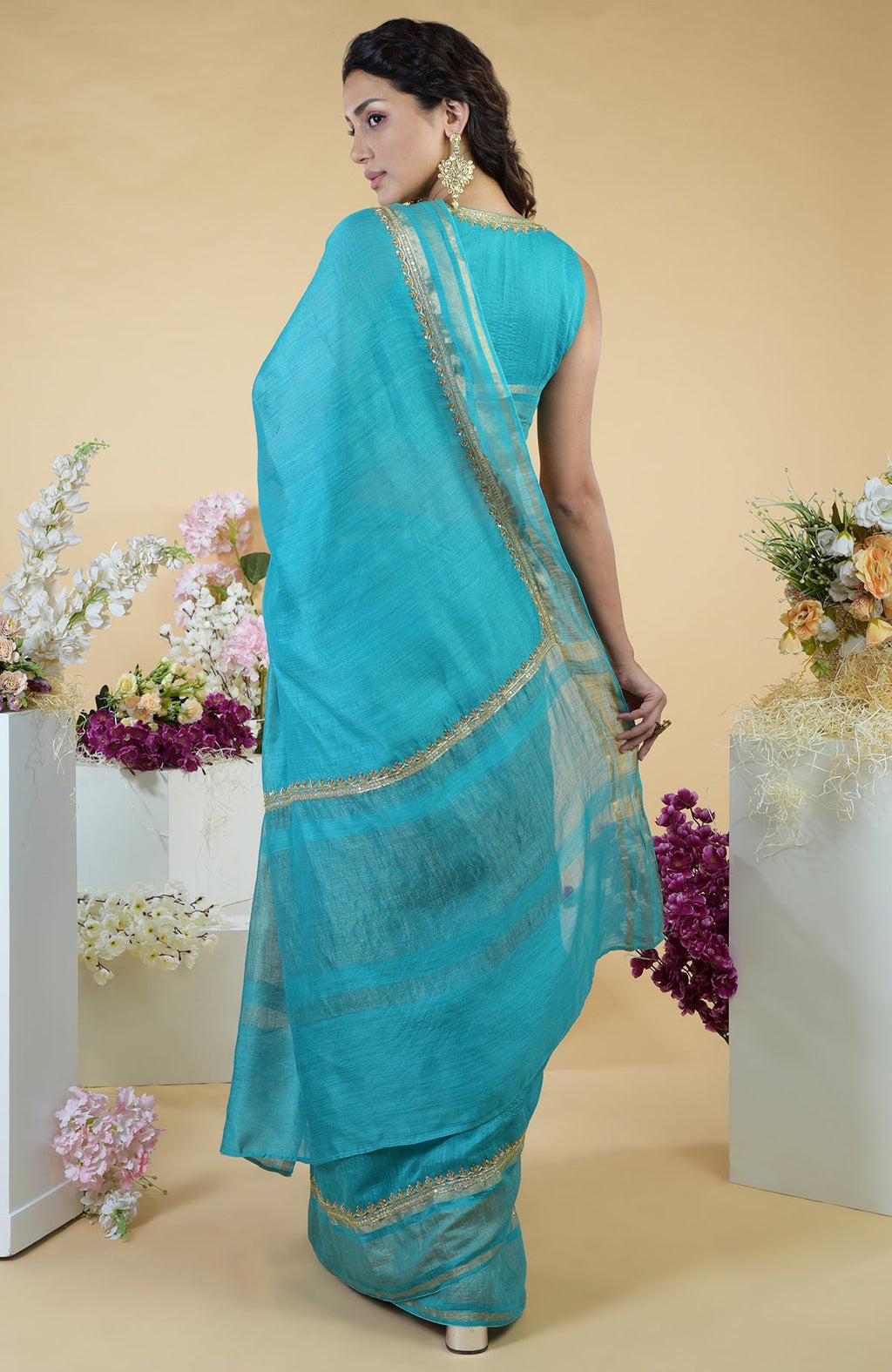 Teal blue linen saree with gold zardozi embroidery and a matching sleeveless blouse.