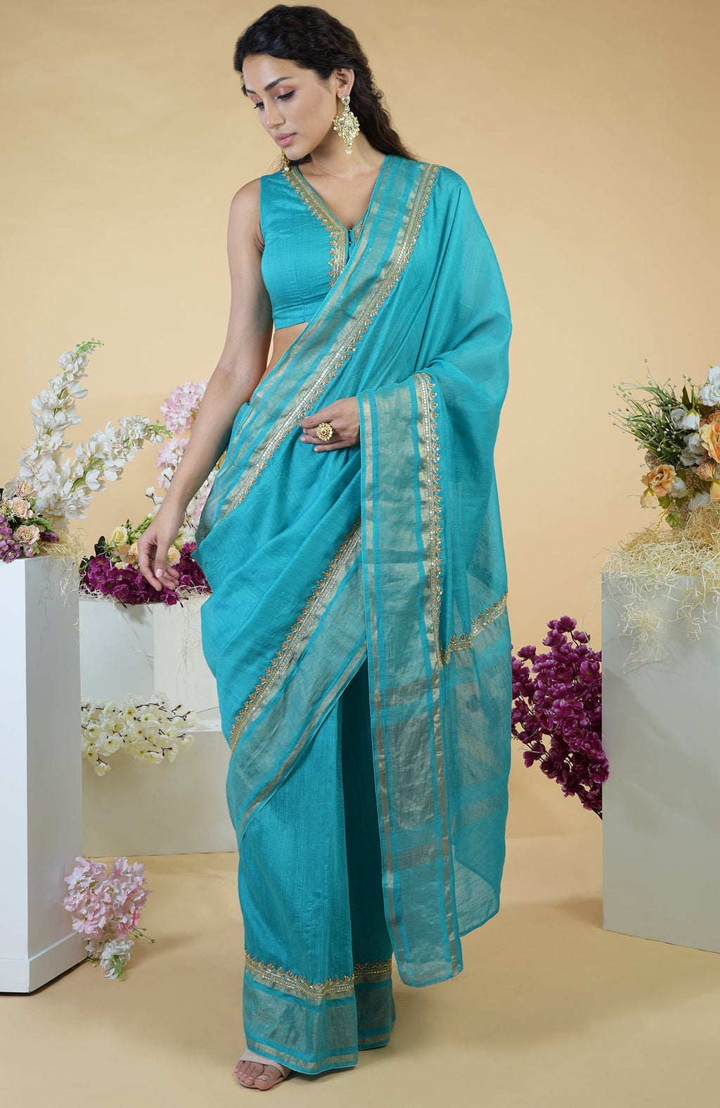 Teal blue linen saree with gold hand embroidery and a matching sleeveless blouse.