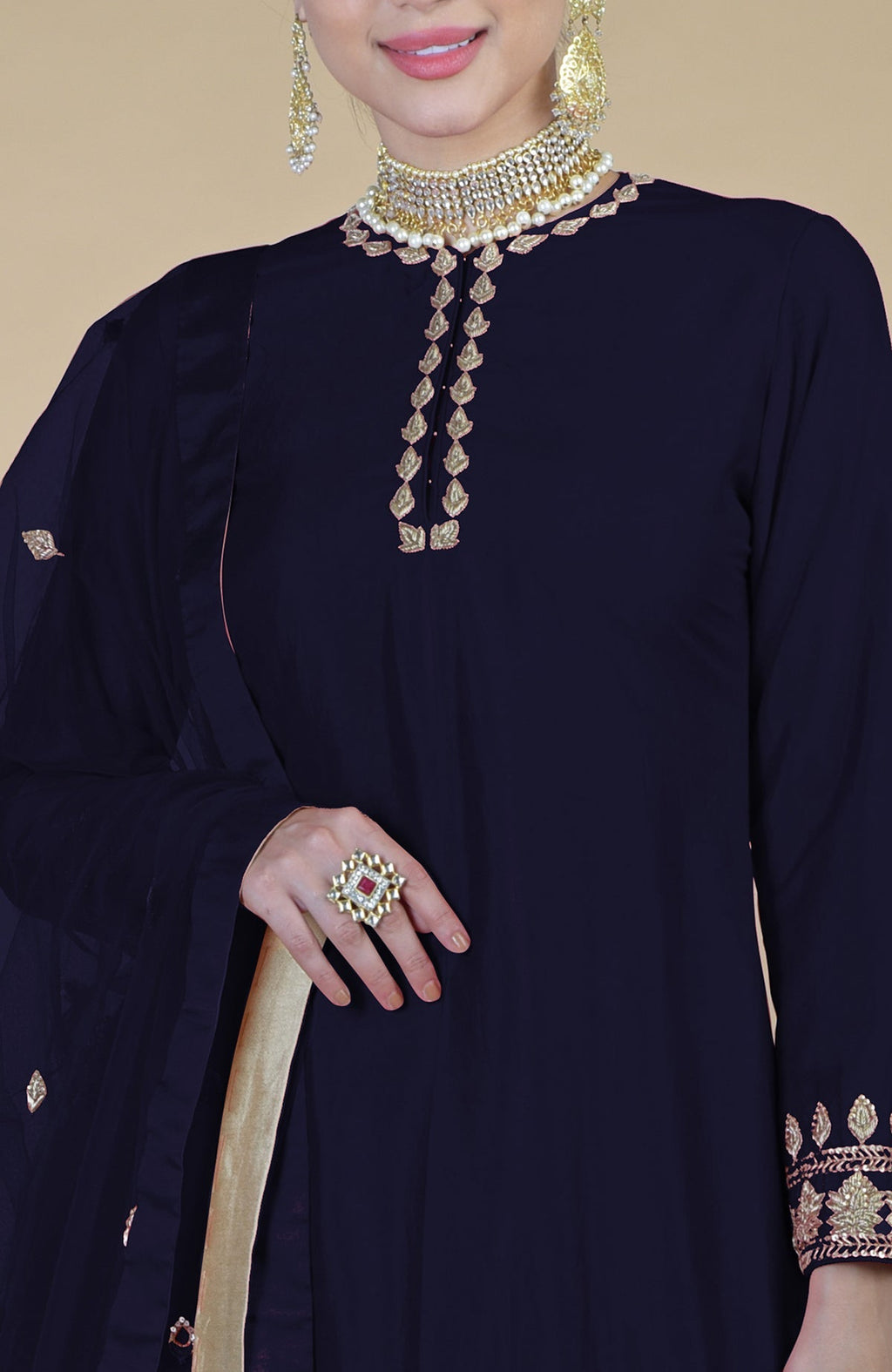 A woman models a midnight blue sharara set with gold embroidery and a statement ring.