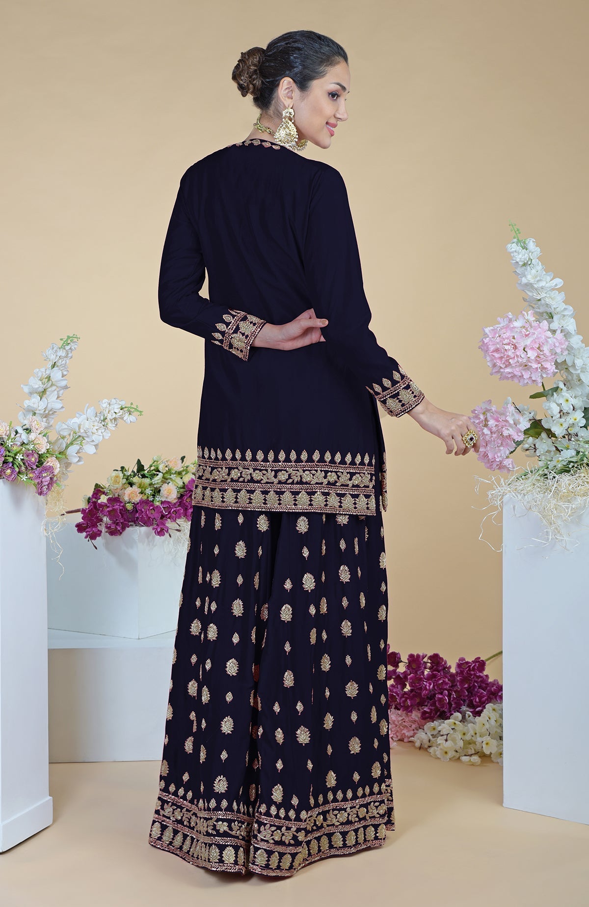 A woman models a midnight blue sharara set with gold embroidery.