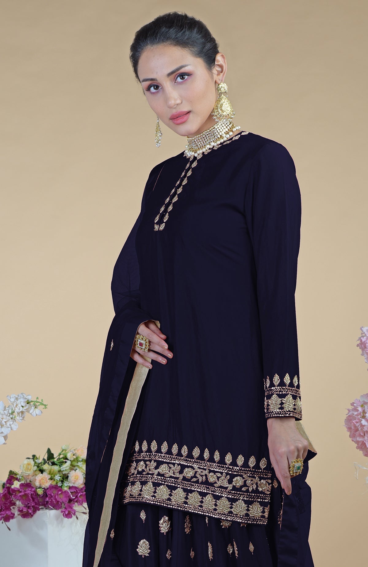 A woman models a midnight blue sharara set with gold embroidery and jewelry.