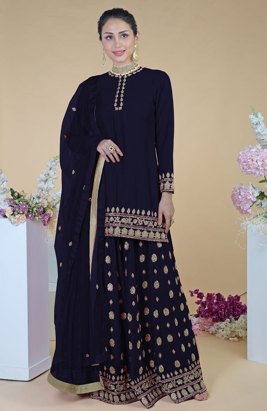 A woman models a midnight blue sharara set with gold embroidery.