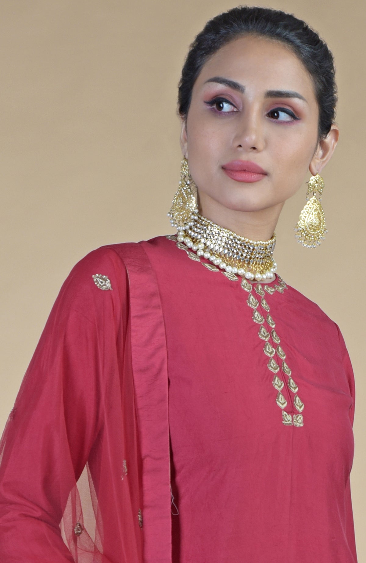 A woman models a crimson sharara set with gold embroidery and a pearl choker.