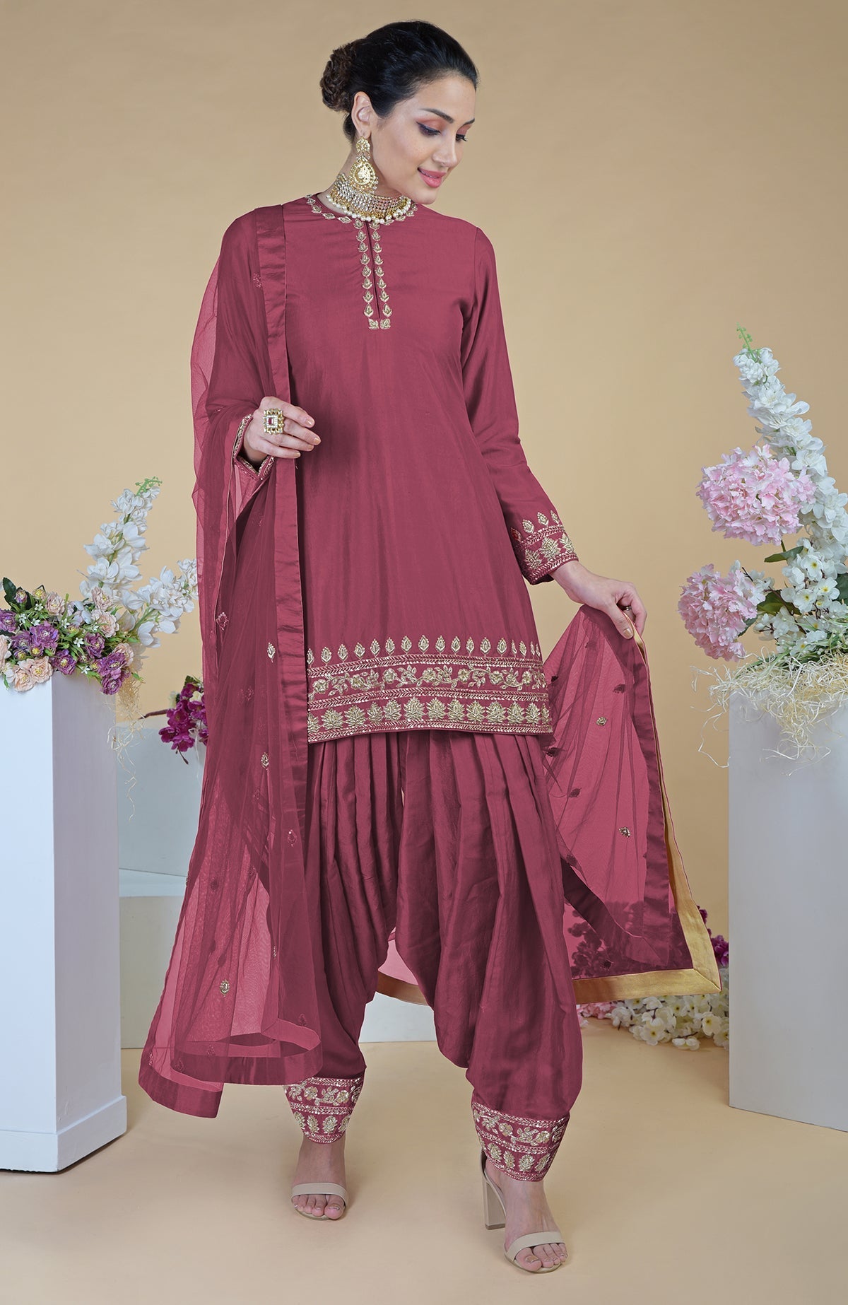 A woman models a maroon salwar suit with gold embroidery and a sheer dupatta.