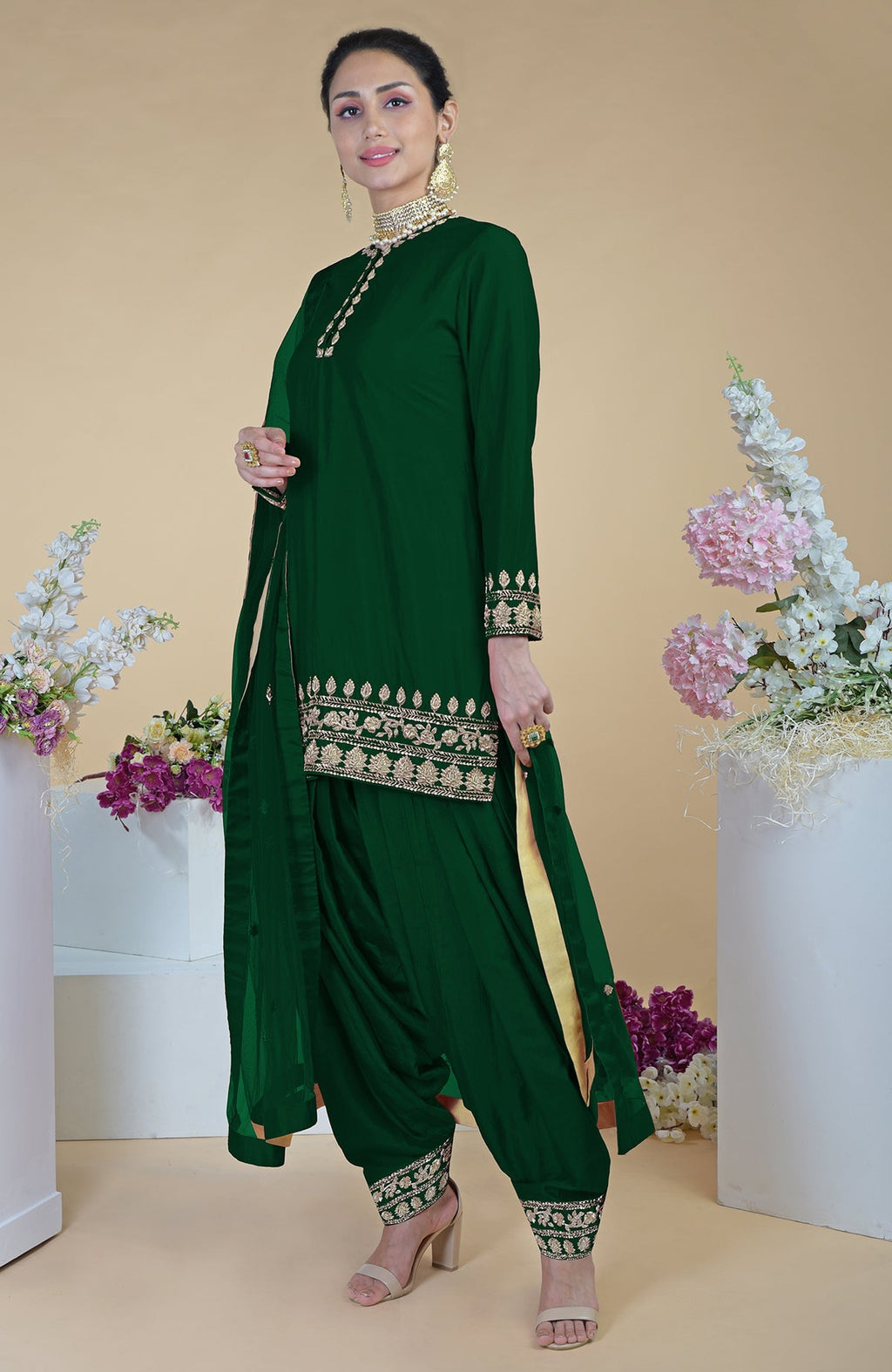 An elegant woman models an emerald green salwar suit with gold embroidery.