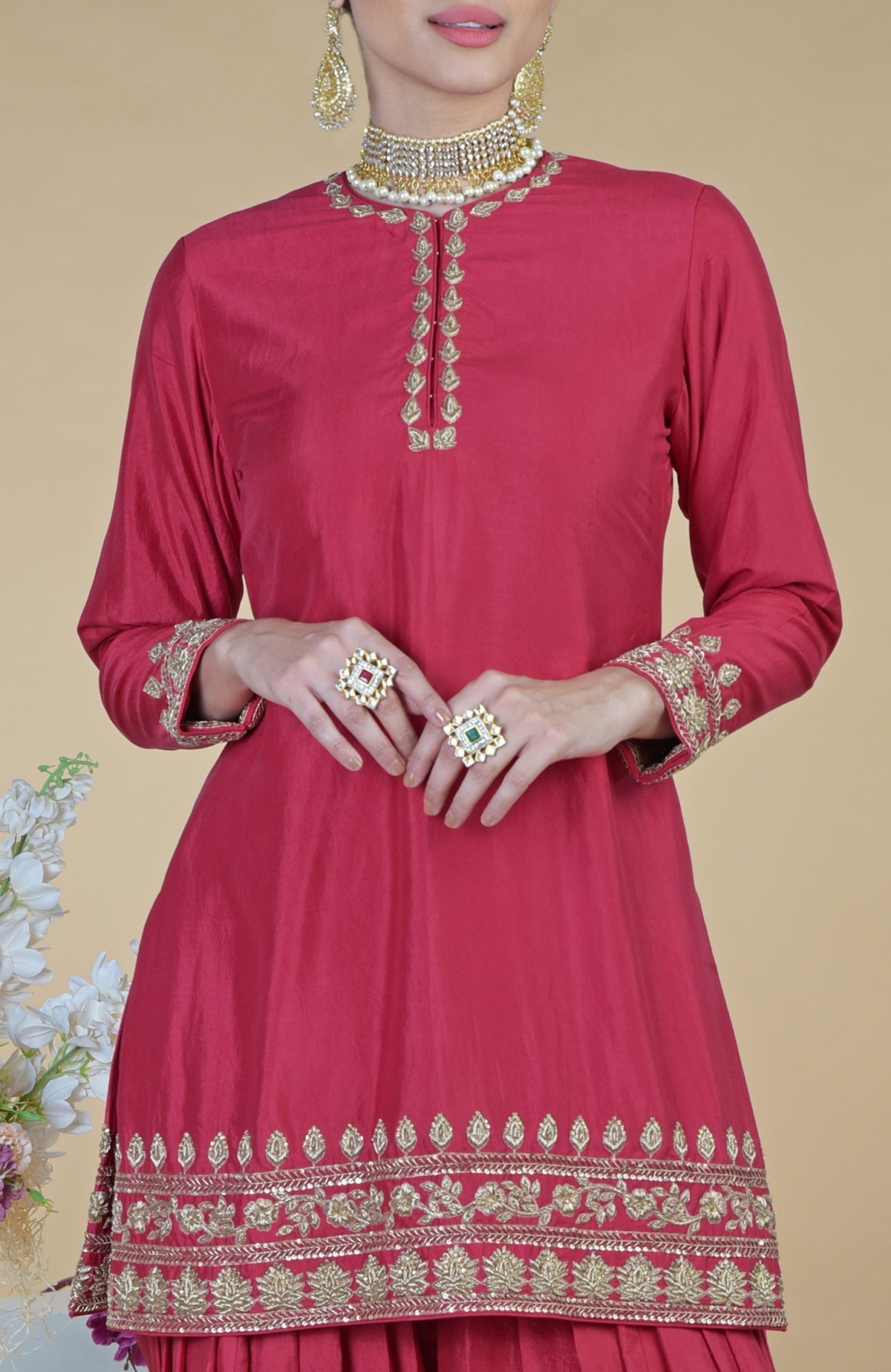 Red salwar suit with gold zardozi embroidery and two large rings.