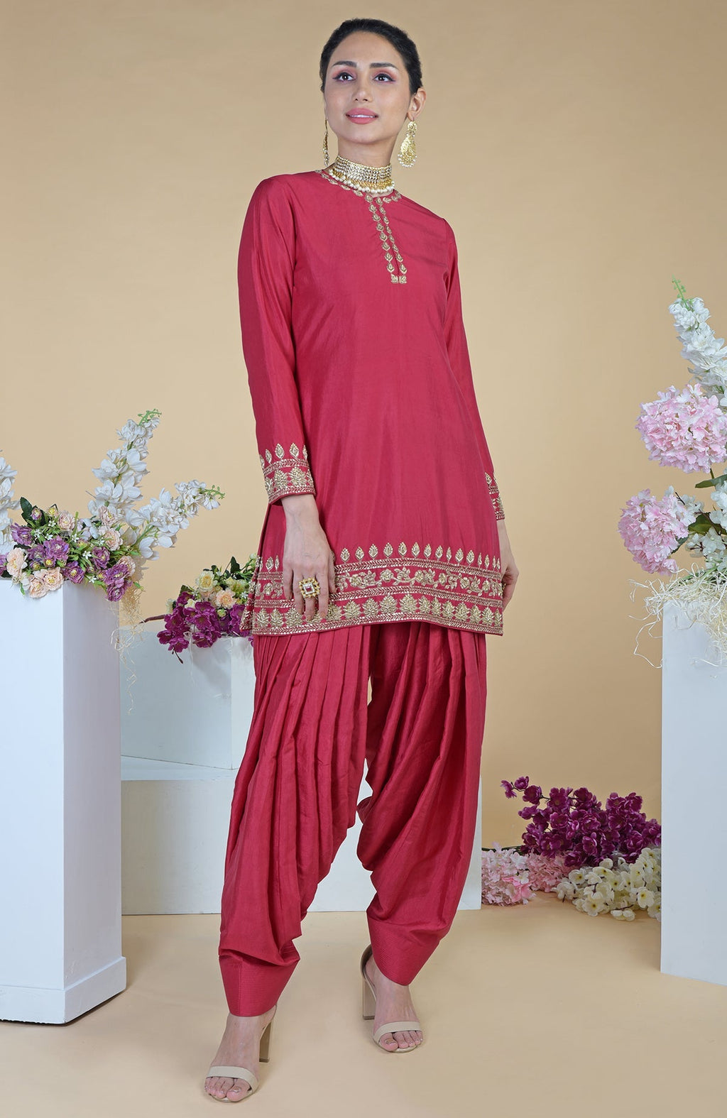 A woman models a red zardozi hand-embroidered salwar suit with gold accents.