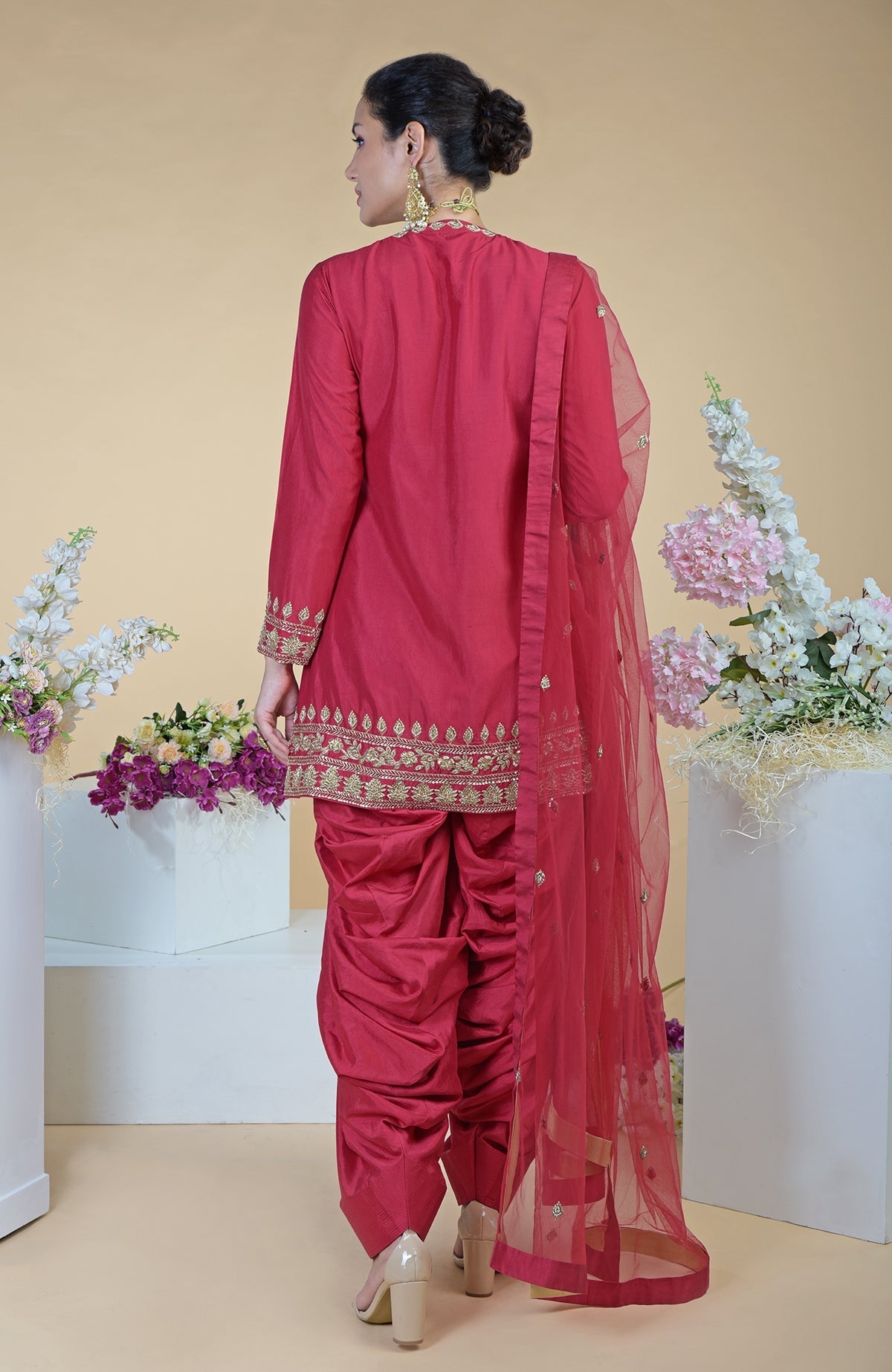 A woman from behind wears a red zardozi hand-embroidered salwar suit with a sheer dupatta.