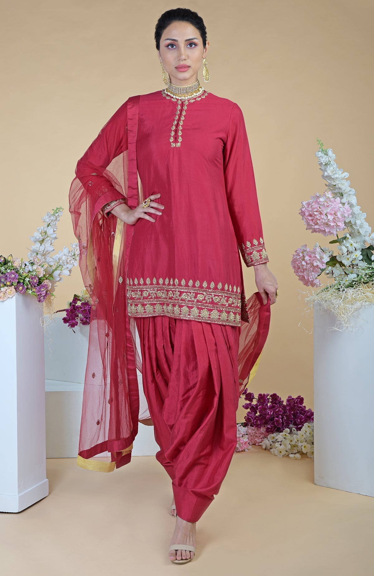 A woman models a red zardozi hand-embroidered salwar suit with a sheer dupatta.
