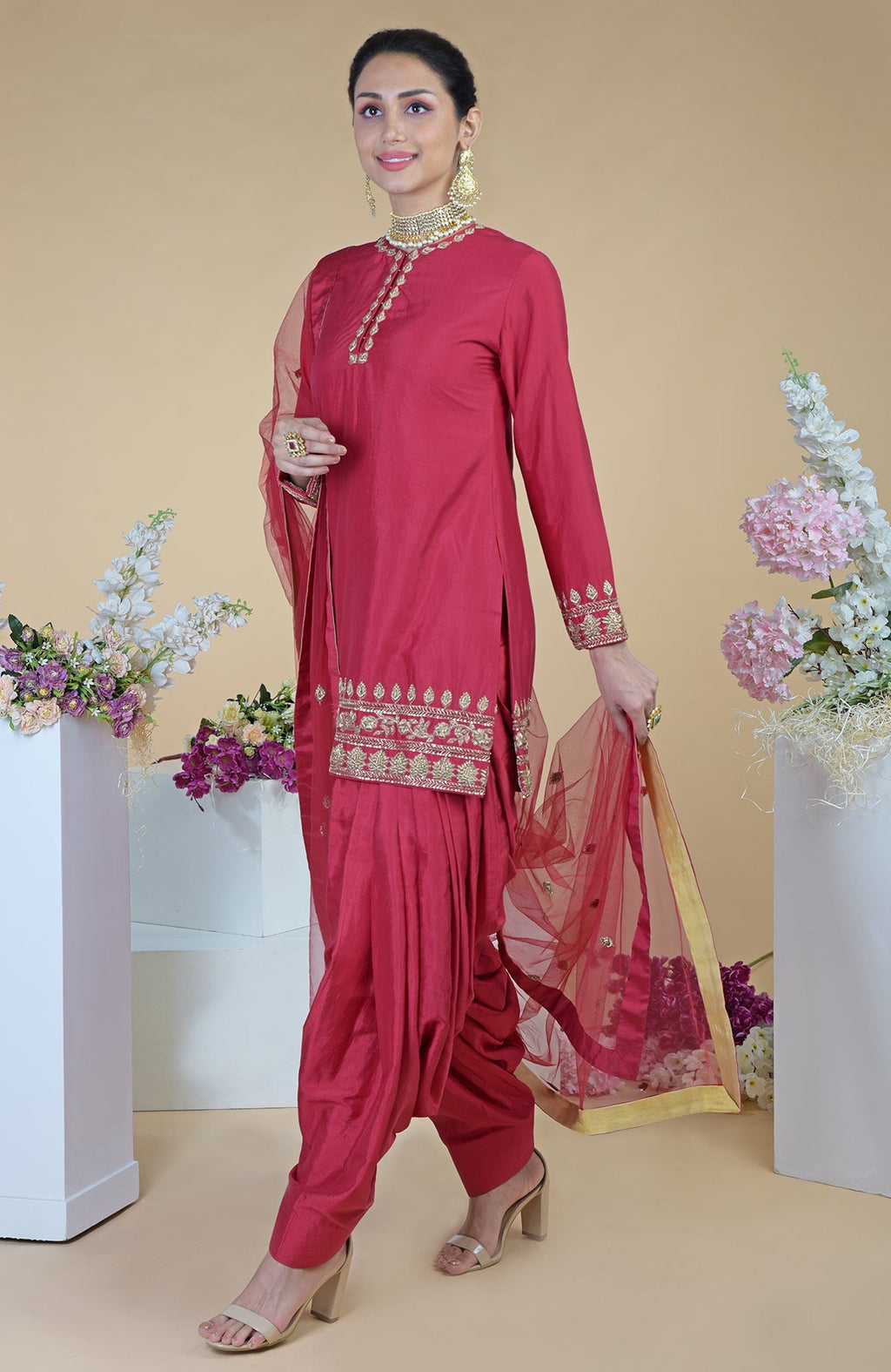 A woman models a red zardozi hand-embroidered salwar suit with a sheer dupatta.