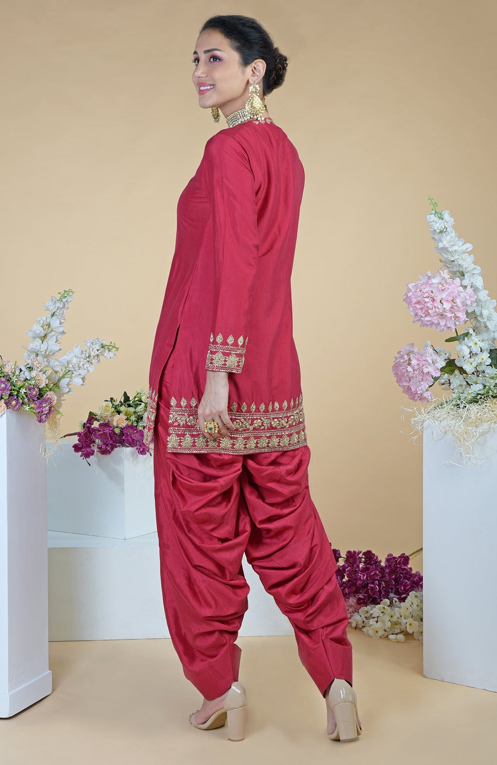 A woman in a red zardozi hand-embroidered salwar suit smiles over her shoulder.
