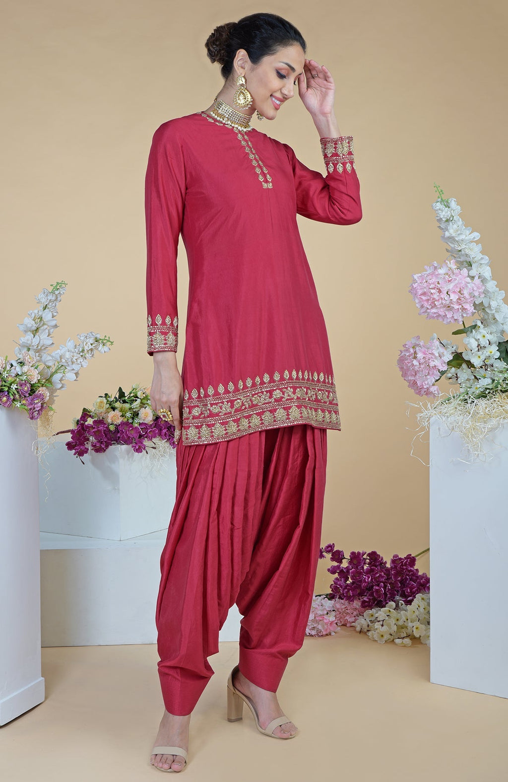 A woman models a red zardozi hand-embroidered salwar suit with gold accents.