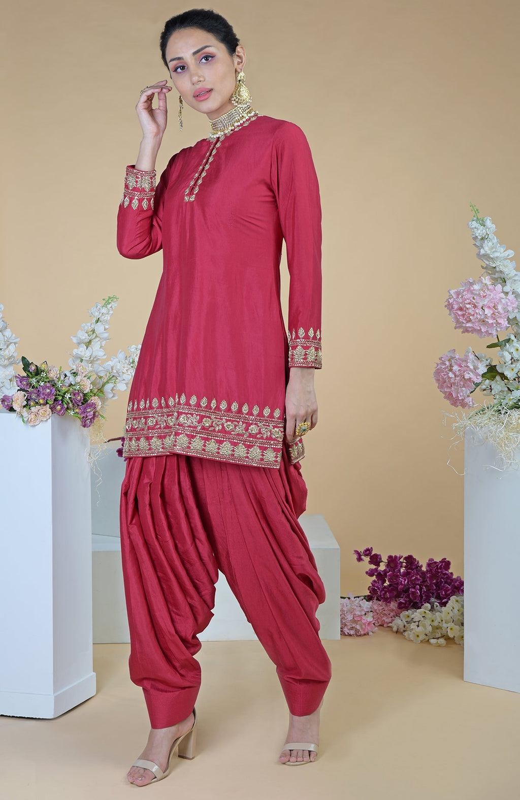 A woman models a red zardozi hand-embroidered salwar suit with gold jewelry.