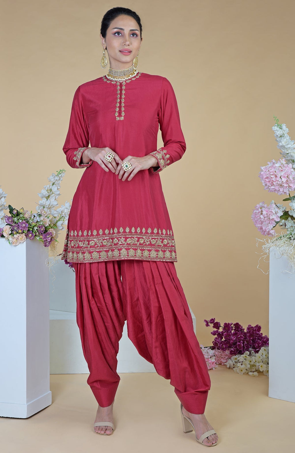 A woman models a red zardozi hand-embroidered salwar suit with gold jewelry.