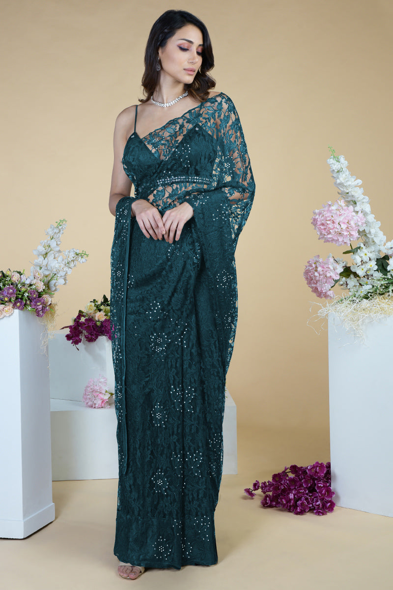 Woman in a dark green lace saree with crystal embellishments.