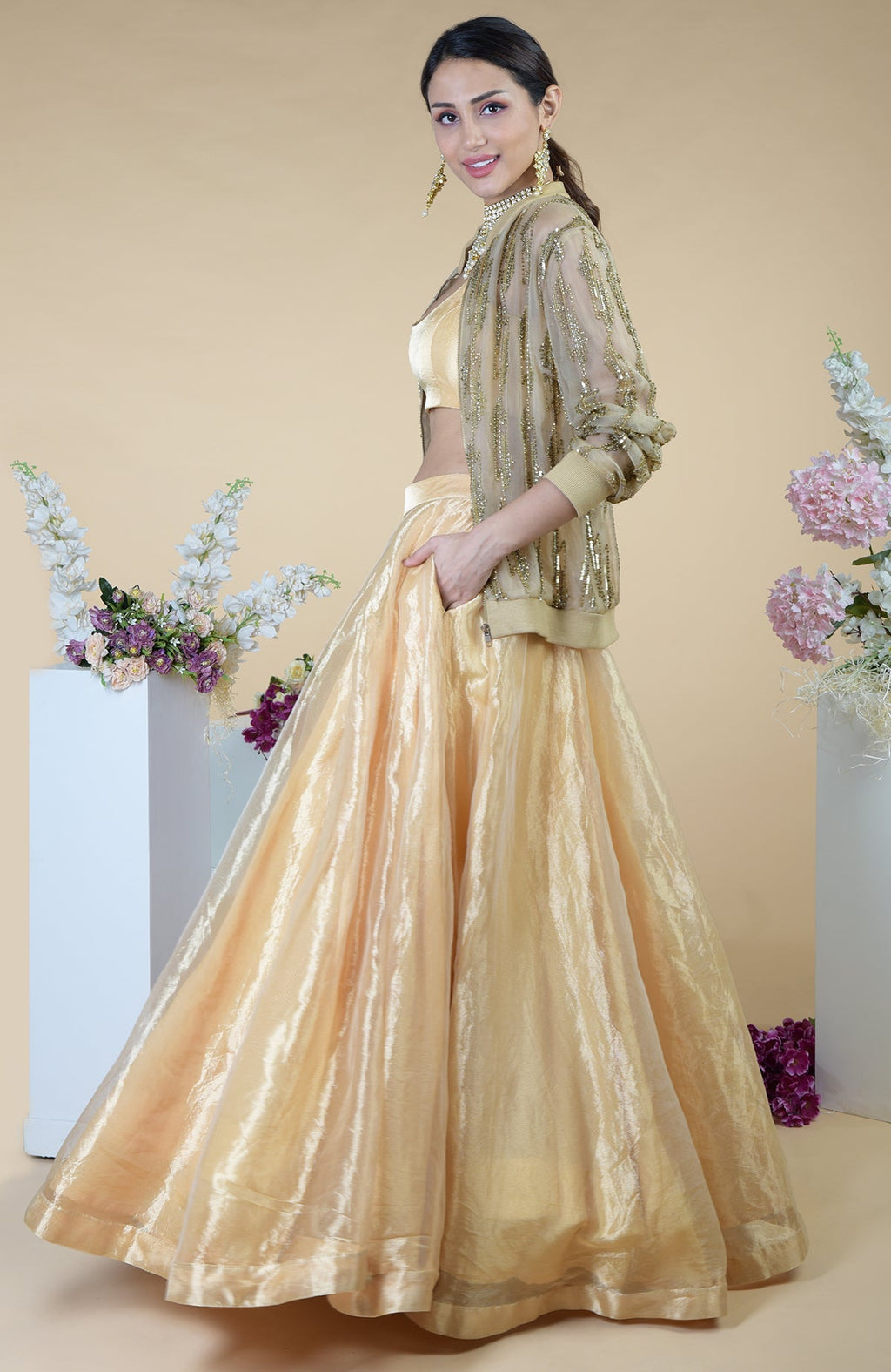 A woman models a gold hand-embroidered cape and skirt set with a matching crop top.