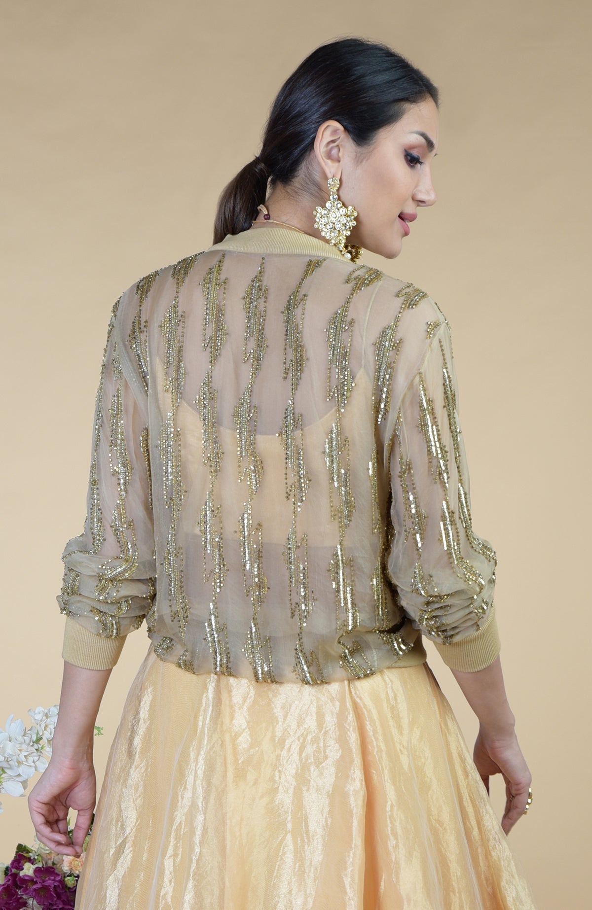 A woman models a sheer gold sequined cape over a matching skirt.