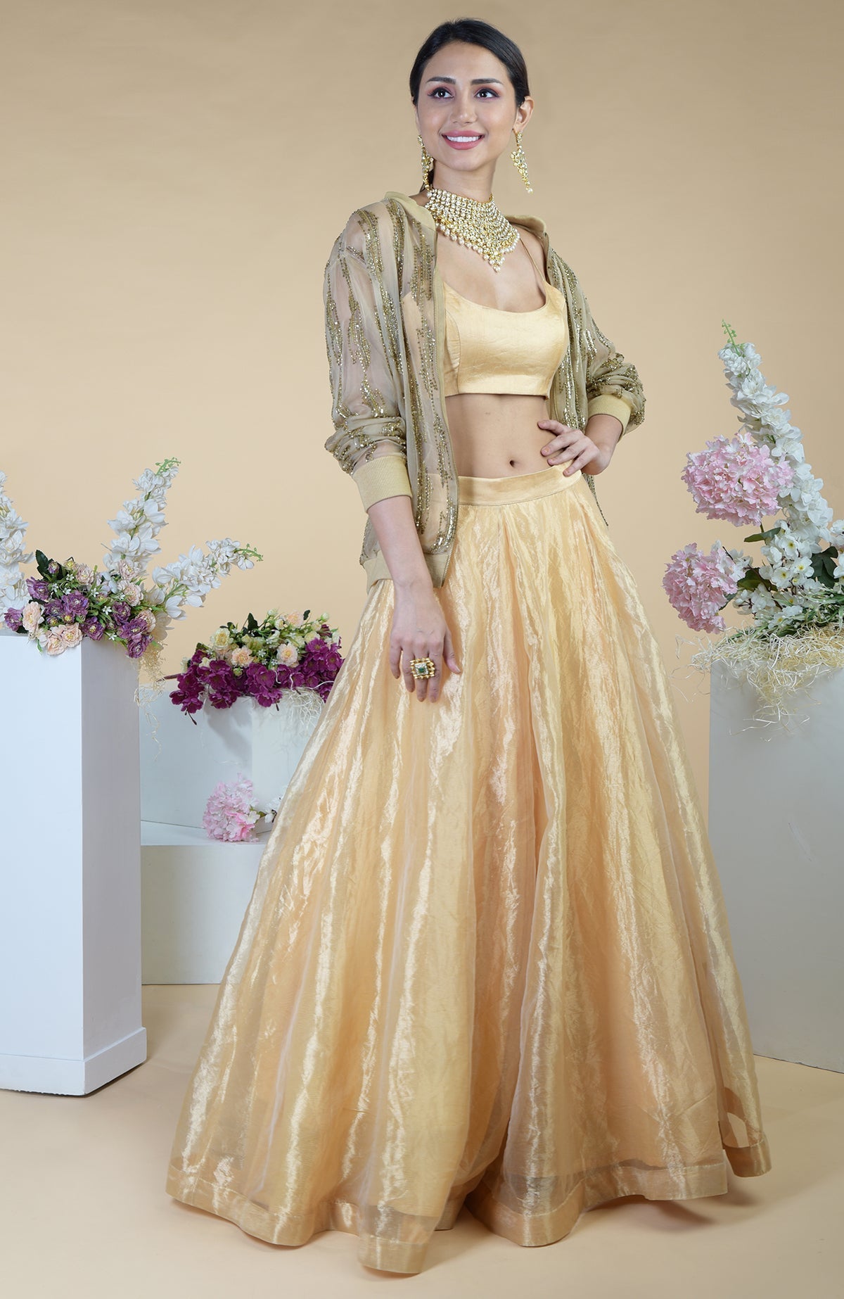 A woman models a gold hand-embroidered cape and skirt set with a matching crop top.