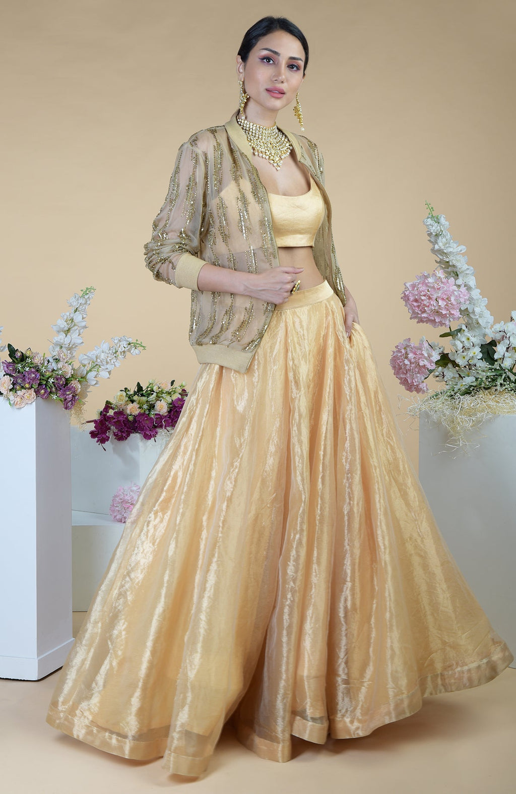 A model wears a gold hand-embroidered cape jacket, matching crop top, and long skirt.