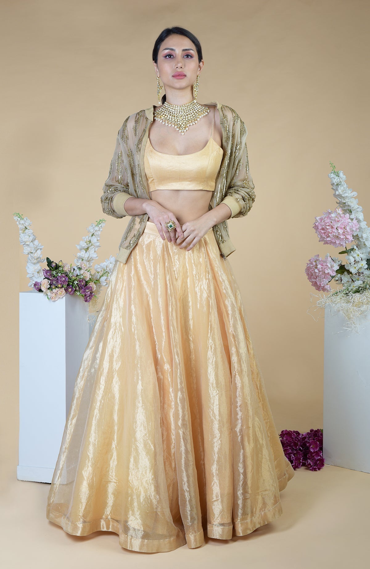 A woman models an embroidered gold jacket, matching crop top, and full skirt.