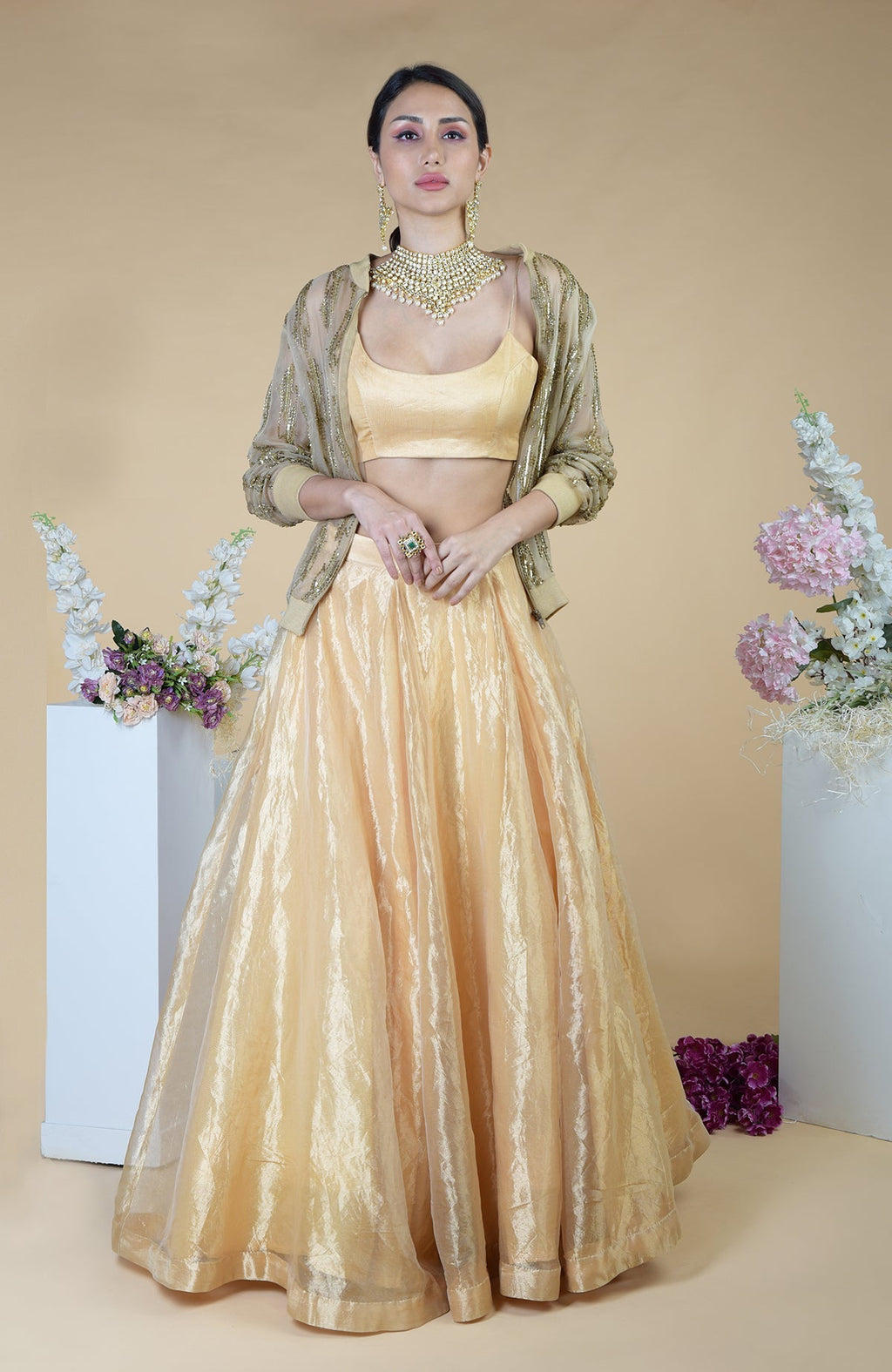 A woman models a gold embroidered cape, matching crop top, and long skirt.