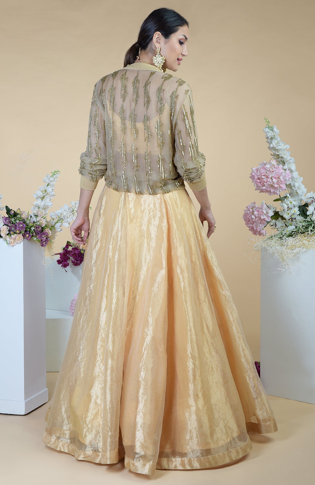 A woman models a gold embroidered jacket and matching skirt set from the back.