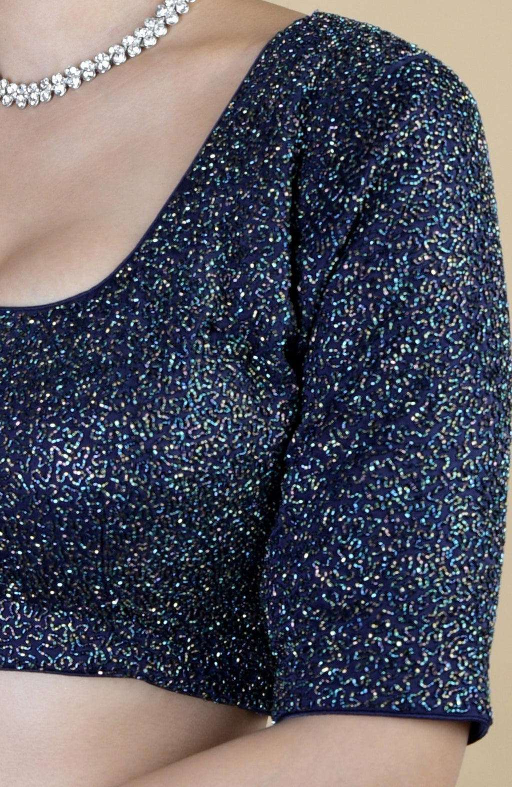 A woman wears a midnight blue sequined blouse with a sparkling necklace.