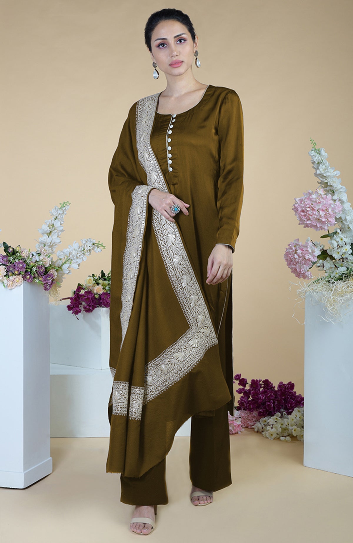 A woman models a brown silk suit with a Tilla embroidered dupatta and white sandals.