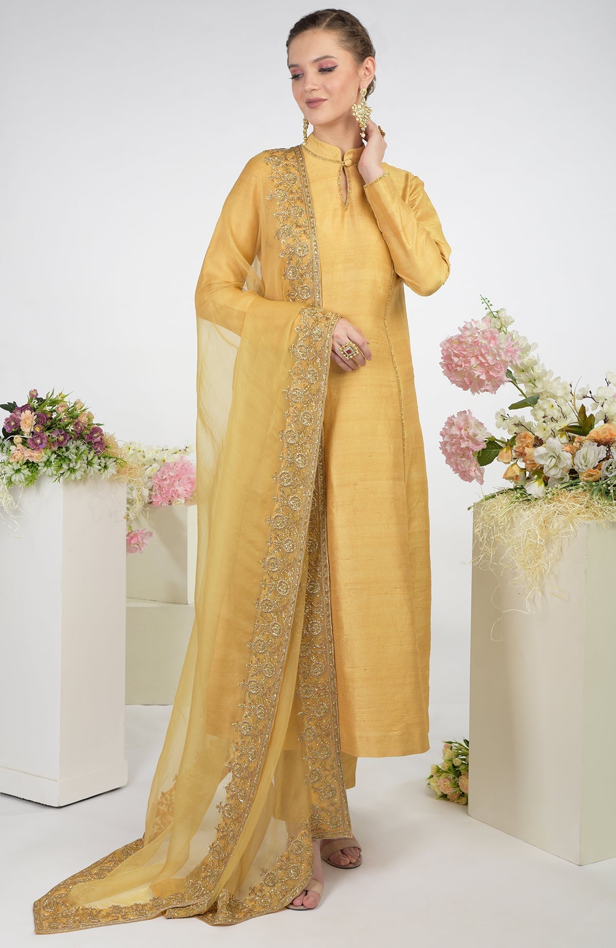 A woman models a gold raw silk kurta set with an embroidered organza dupatta.