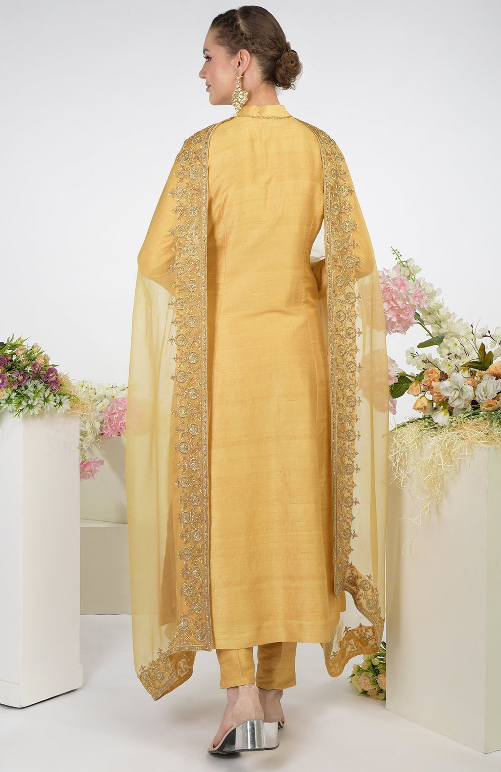 A woman models a gold raw silk kurta set with an embroidered organza dupatta.