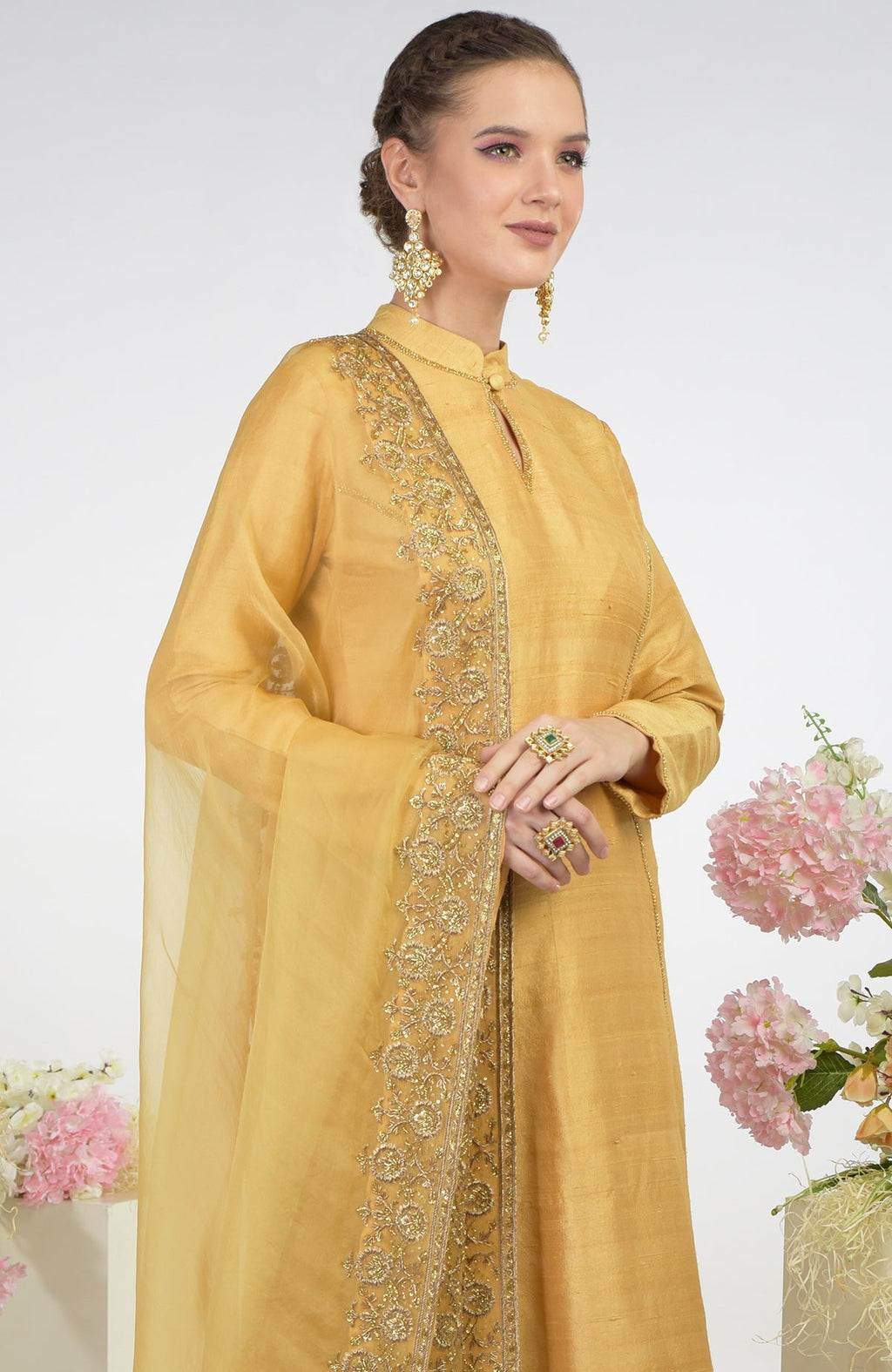 A woman models a gold raw silk kurta set with an embroidered organza dupatta.