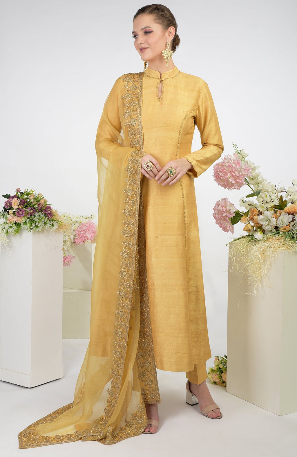 A woman models a gold raw silk kurta set with an embroidered organza dupatta.