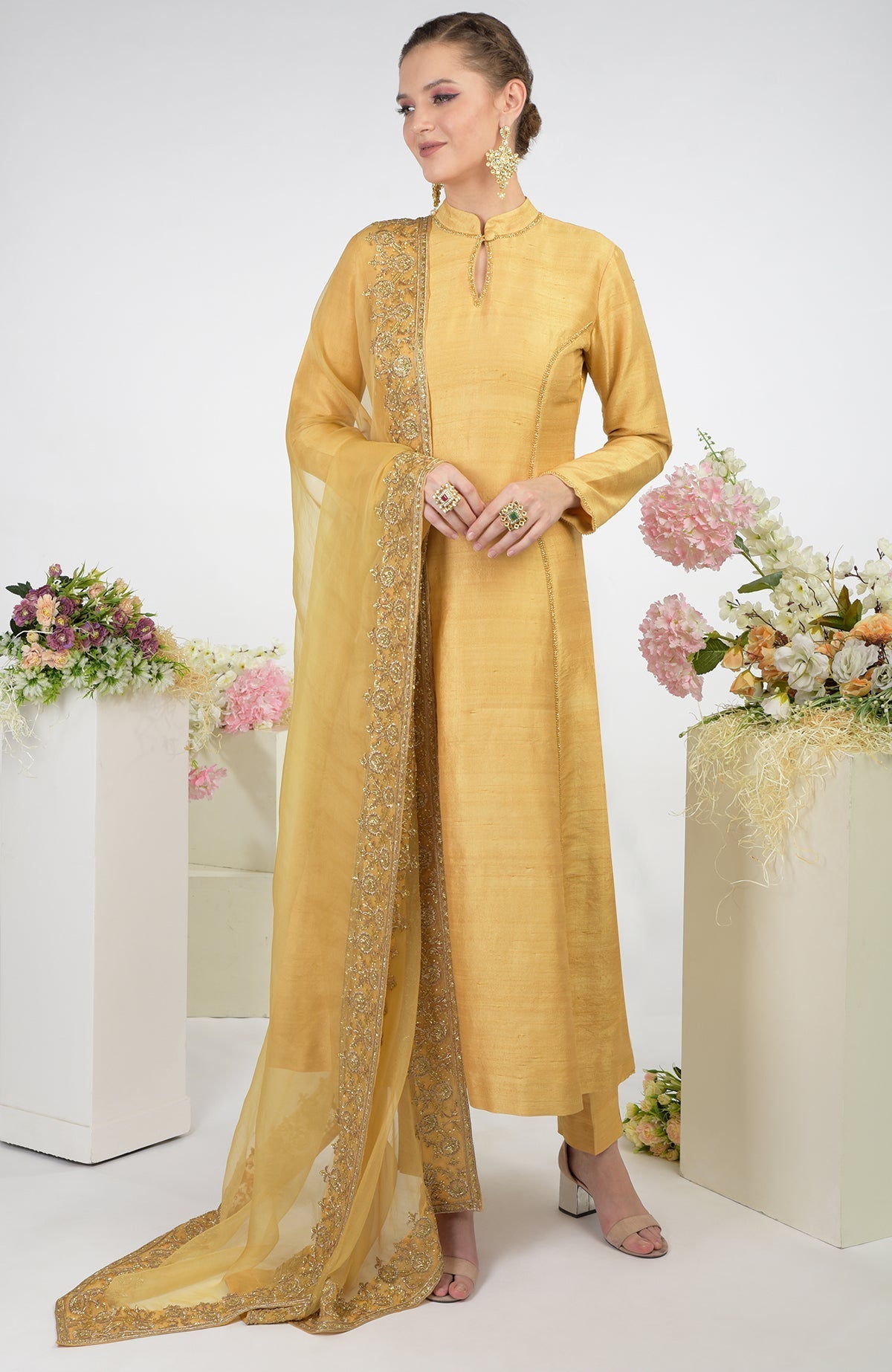 A woman models a gold raw silk kurta set with an embroidered organza dupatta.