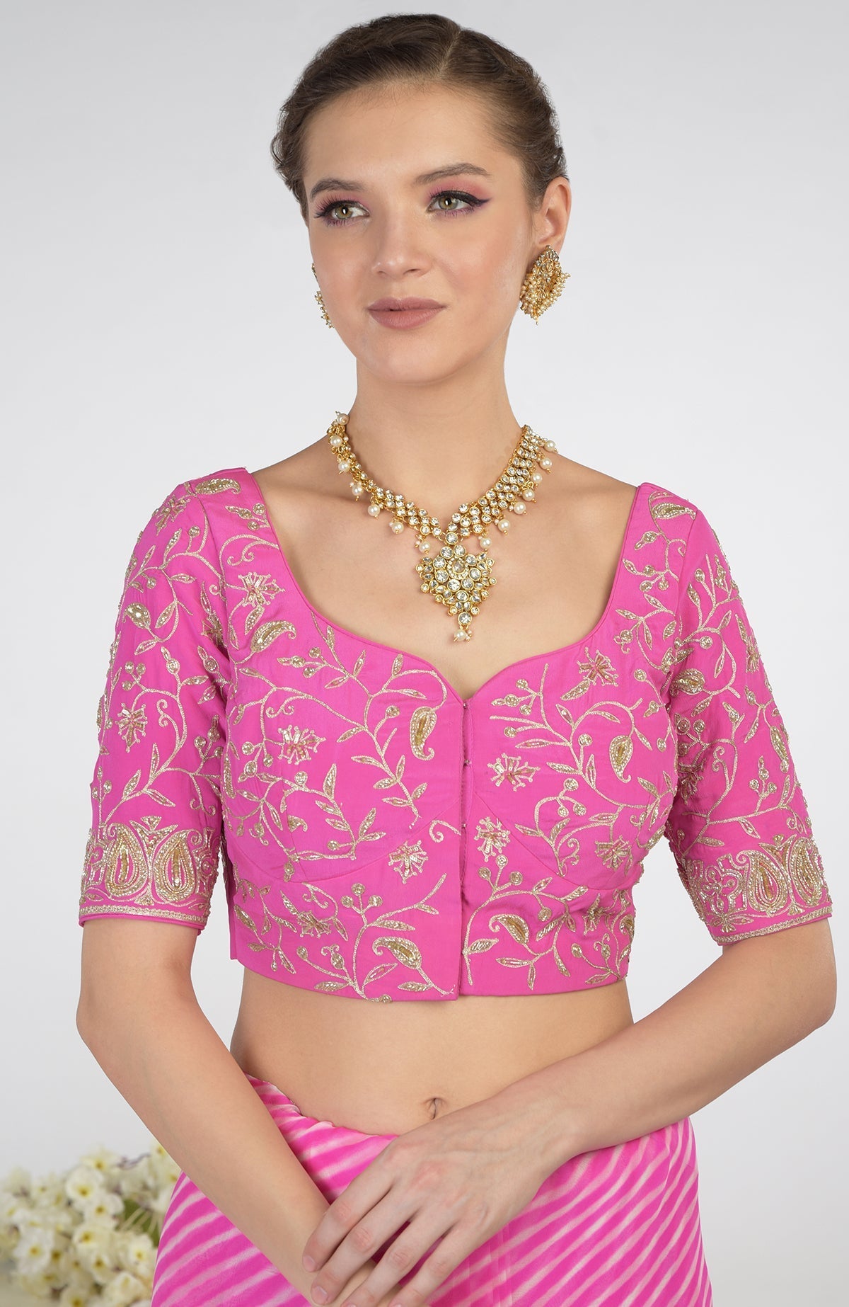A woman models a pink leheriya saree with a matching embroidered blouse and jewelry.