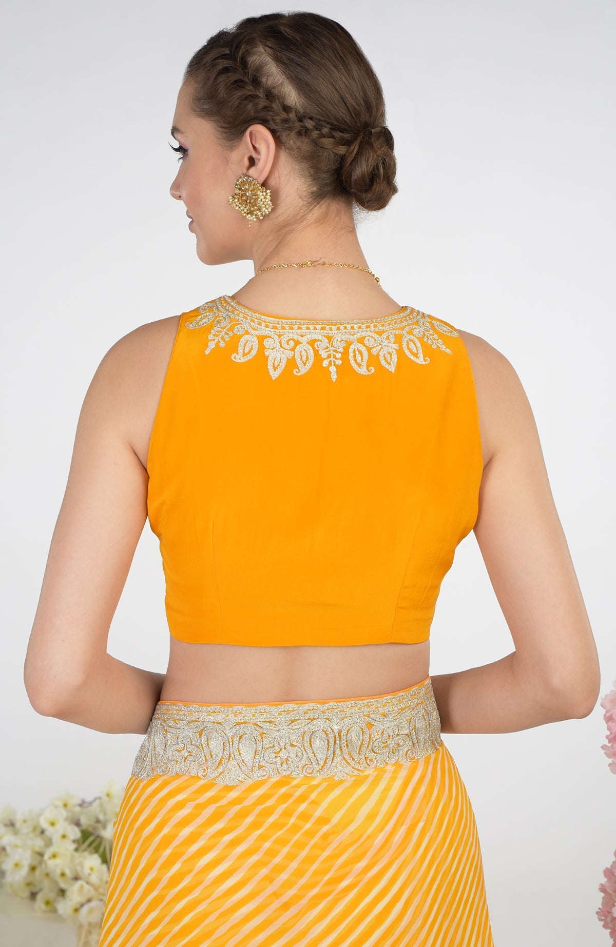 A woman from the back wearing a yellow leheriya saree with a tilla aari embroidered blouse.