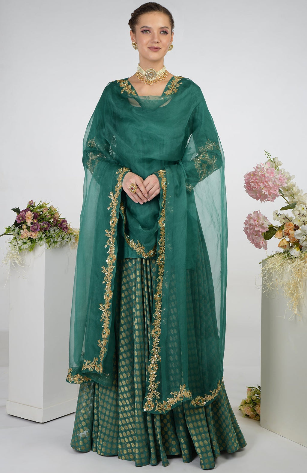 A woman models a bottle green Banarasi Zardozi Kalidaar skirt set with gold embroidery.