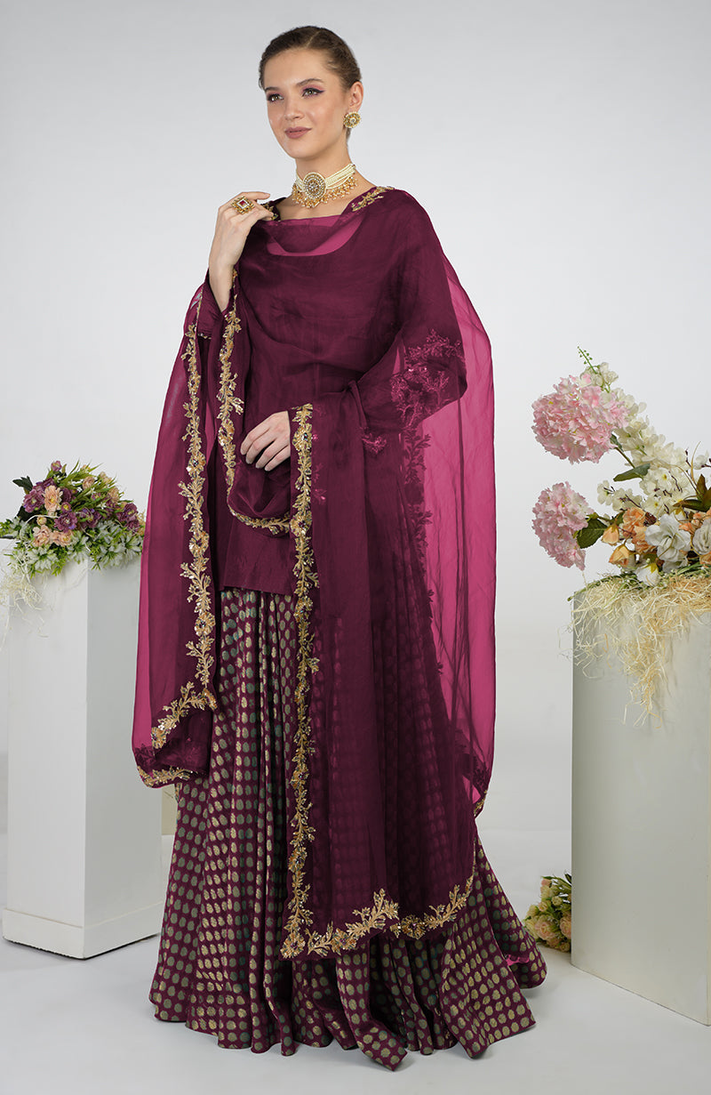 A woman models an amethyst Banarasi Zardozi Kalidaar skirt set with gold embroidery.